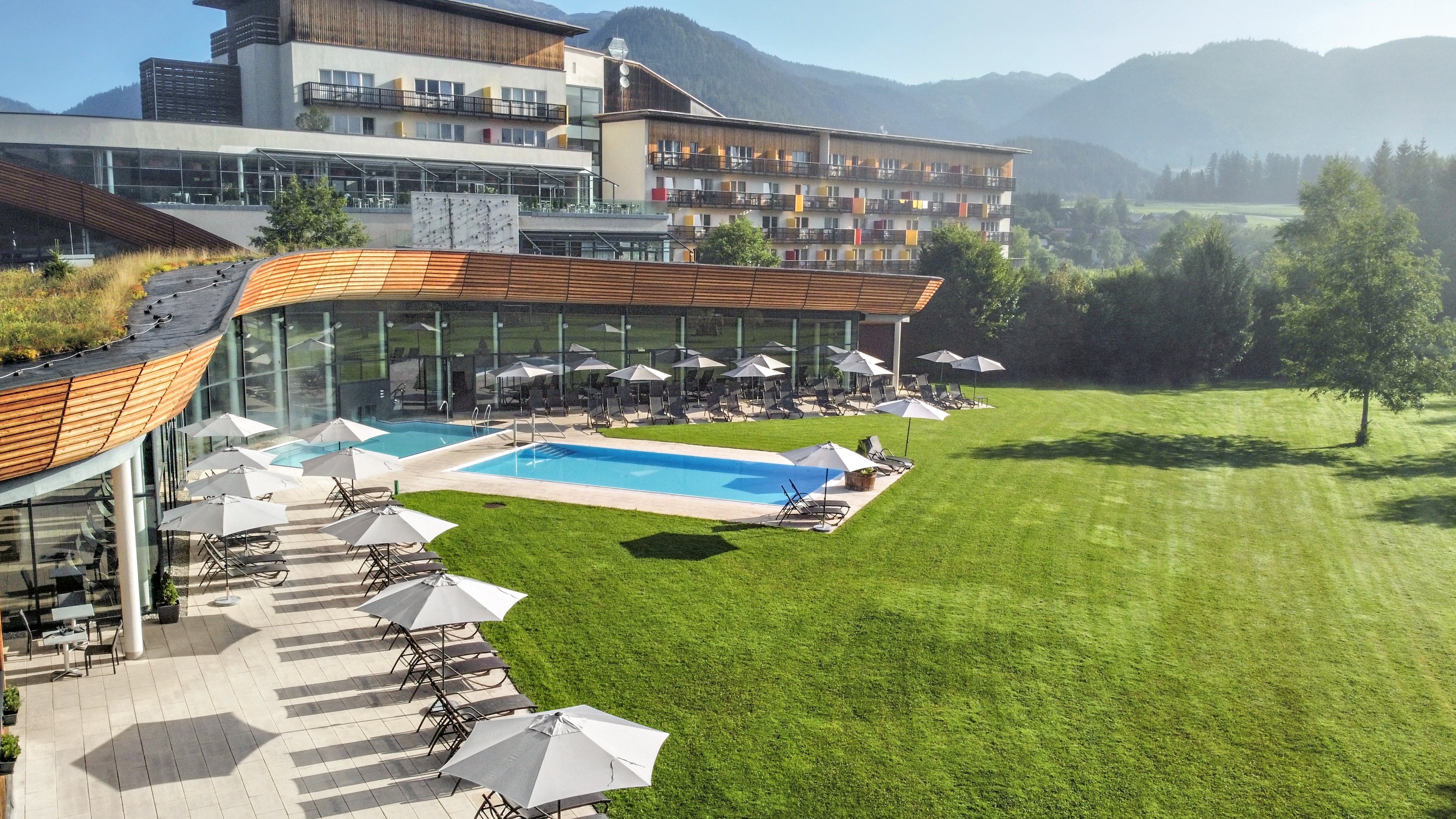 Ansicht eines Aldiana Clubhotels mit Pool, Liegen und grünem Garten, im Hintergrund Berge