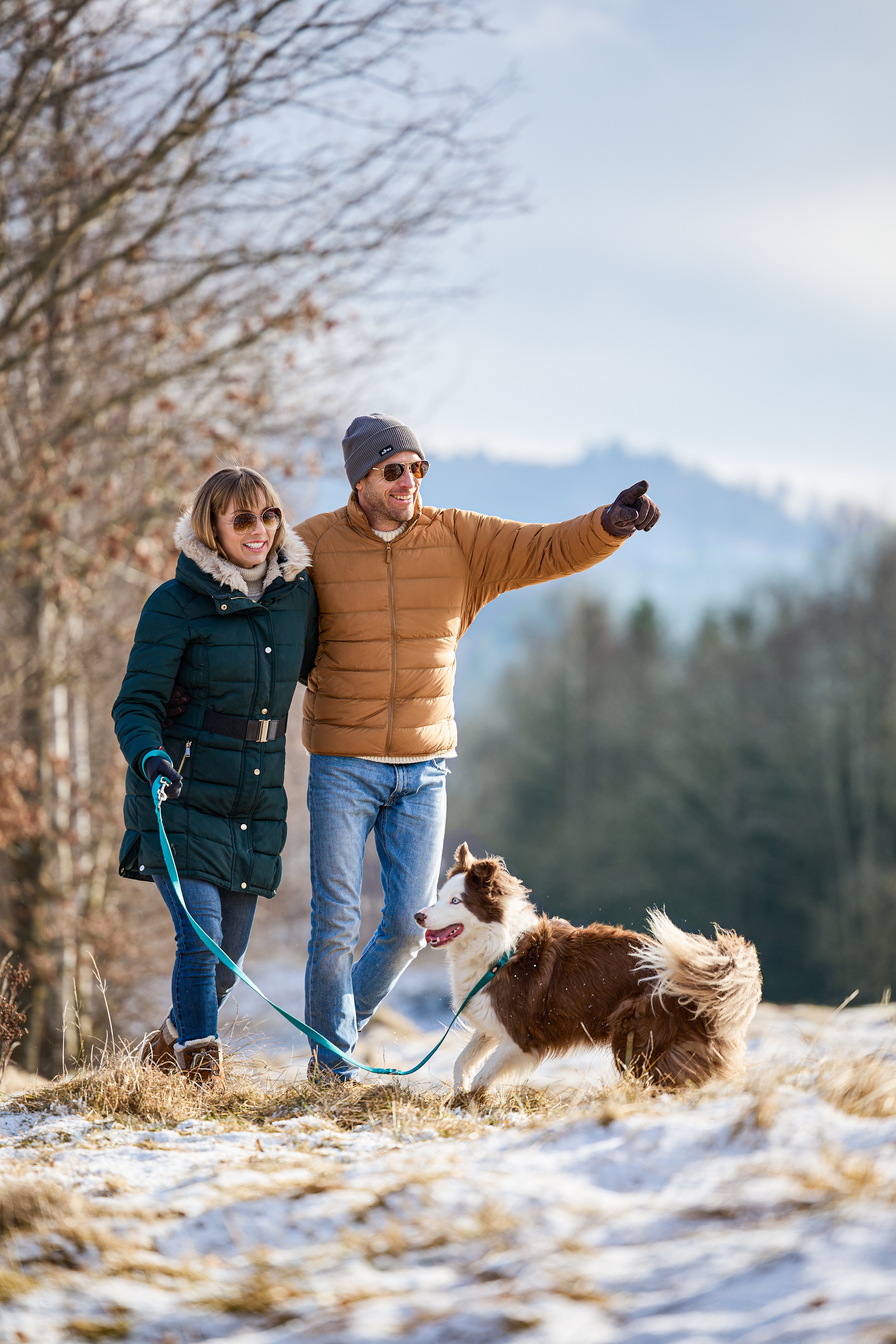 Zwei Menschen mit Hund im Schnee, genießen einen Winterspaziergang in der Natur