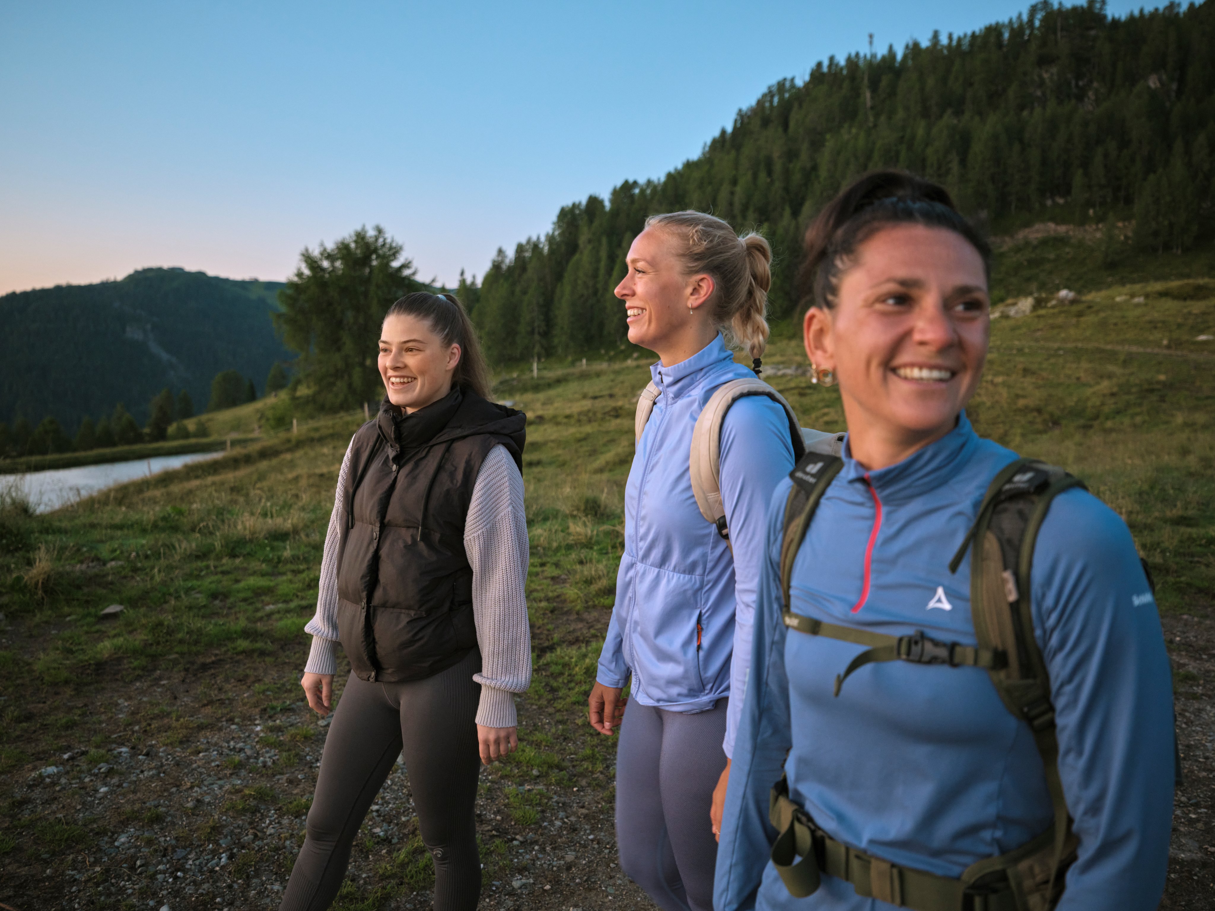 Drei Wanderer mit Rucksäcken in einer grünen Berglandschaft bei Sonnenaufgang