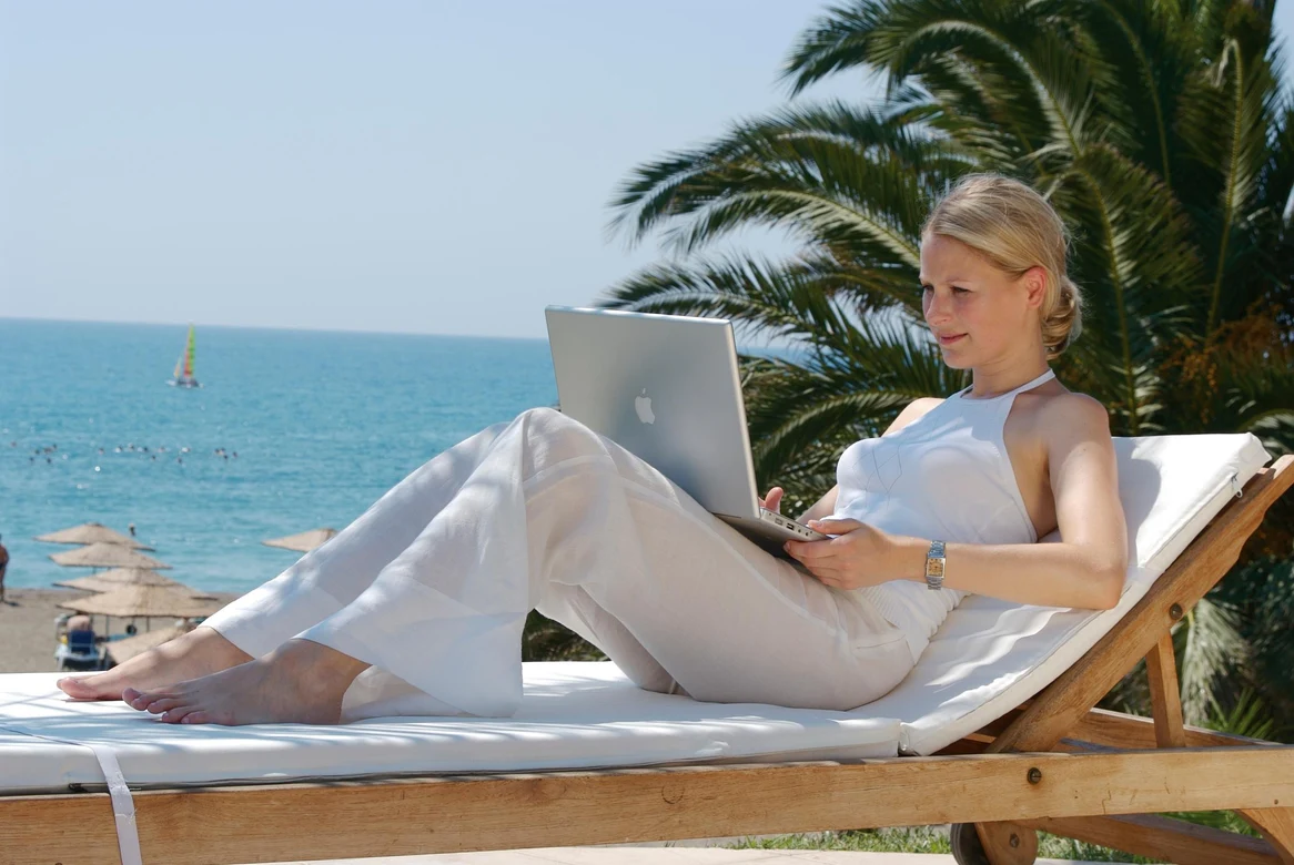 Frau entspannt auf Liege am Strand mit Laptop und Sonnenschutz, Premium Cluburlaub bei Aldiana