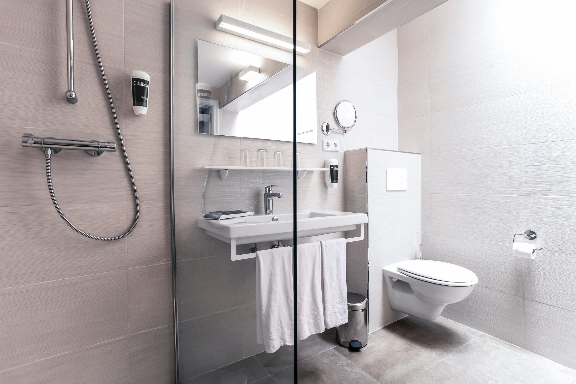 Badezimmer mit Spiegel, Waschbecken, Toilette und Dusche bei Aldiana, barrierefrei.