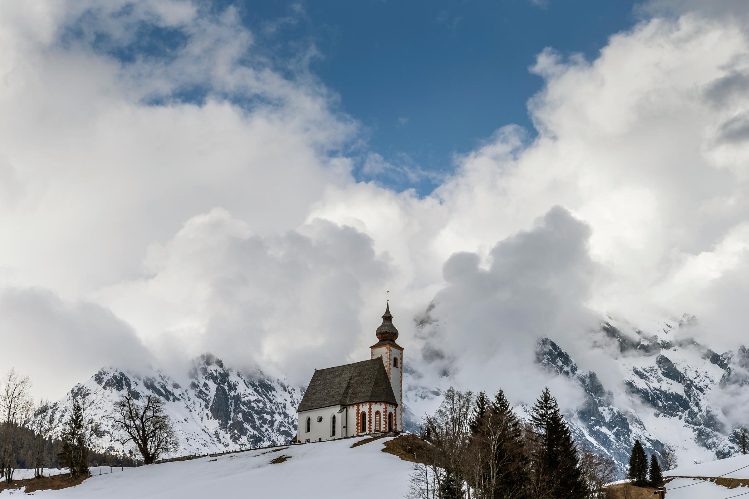 Ein weißes Gebäude mit Kirchturm vor verschneiten Bergen, eleganter Cluburlaub bei Aldiana