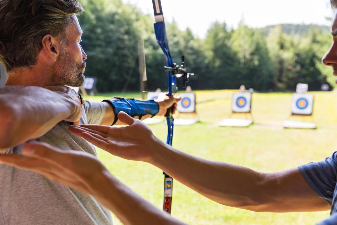 Mitarbeiter weist Gast beim Bogenschießen ein