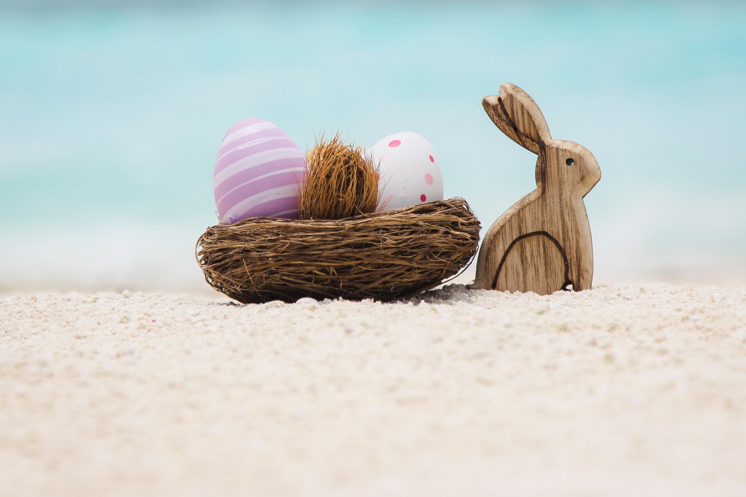 Vier Ostereier, ein Nest und ein Holzhasen auf Sand, symbolisieren Frühlingsfreude bei Aldiana