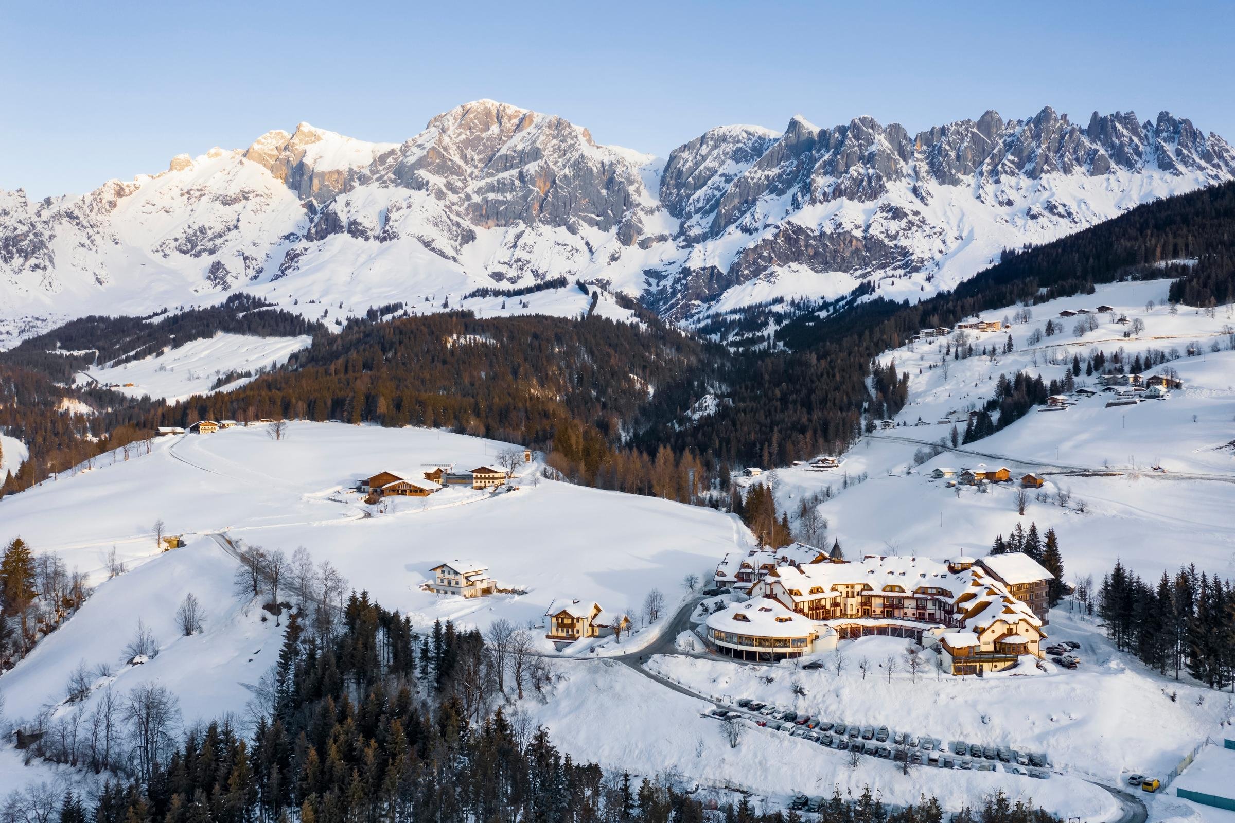 Buntes Winterpanorama mit verschneiten Bergen, Gebäuden und Tannen im Alpenurlaub