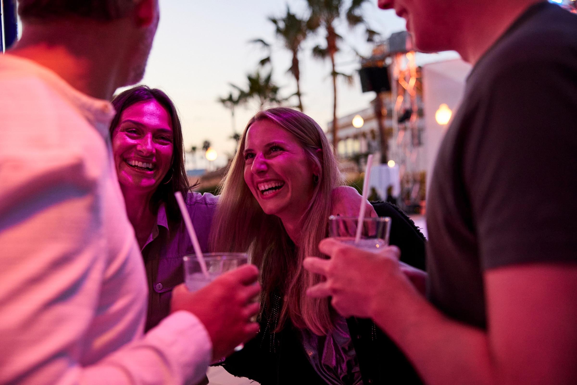Mehrere Menschen bei einem geselligen Treffen, bei Sonnenuntergang am Strand, trinken Cocktails