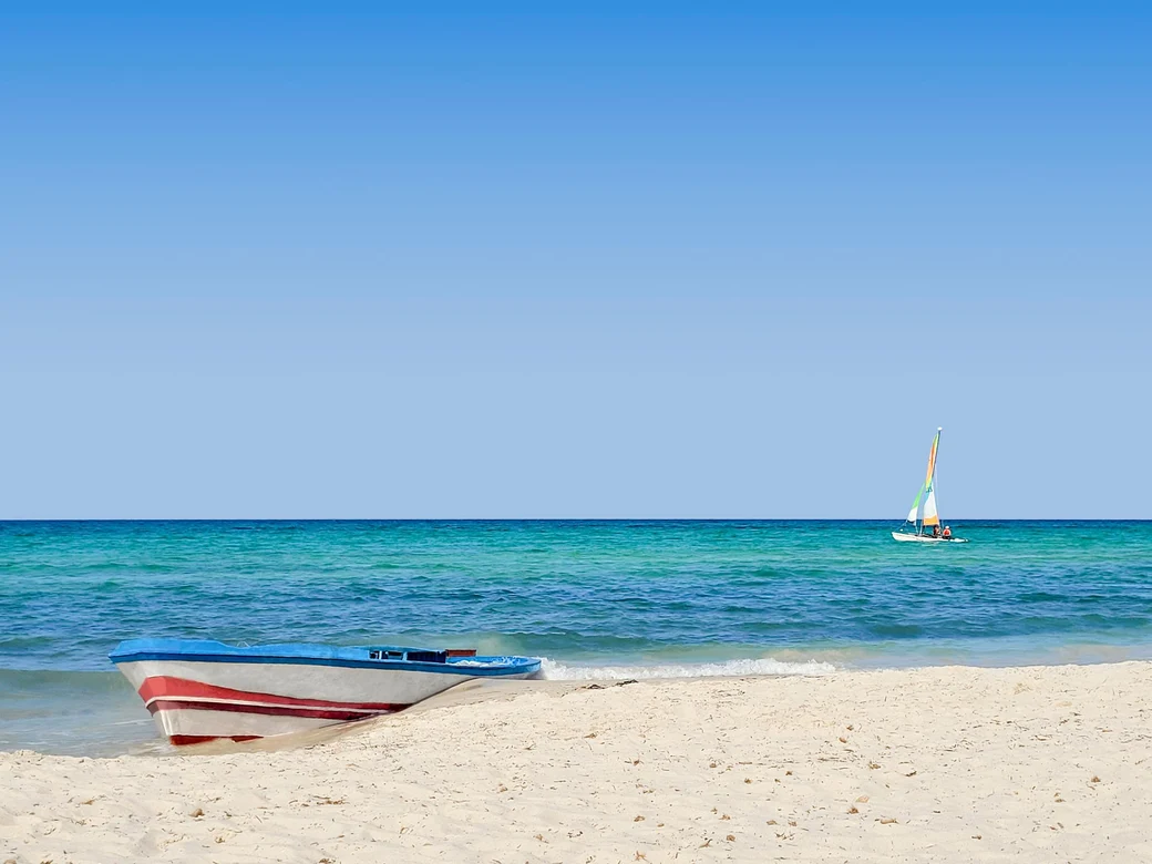 Blick auf einen weißen Strand mit Booten und klarem blauen Himmel bei Aldiana Premium Cluburlaub