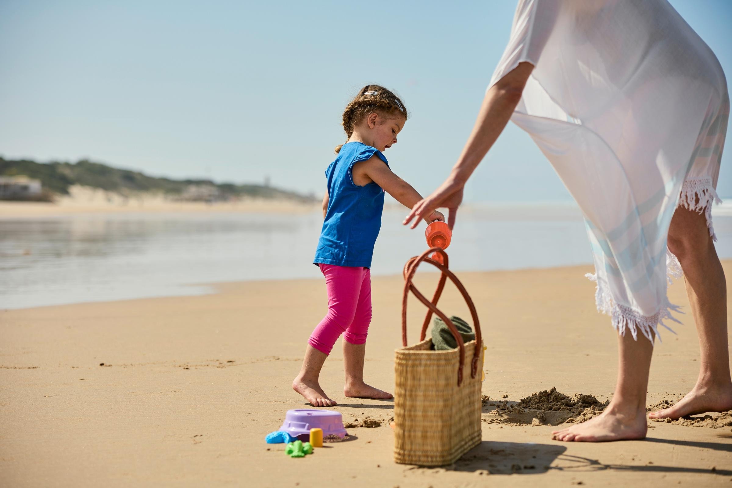Ein Kind spielt am Strand mit einer Erwachsenenfigur, die eine Strandtasche trägt