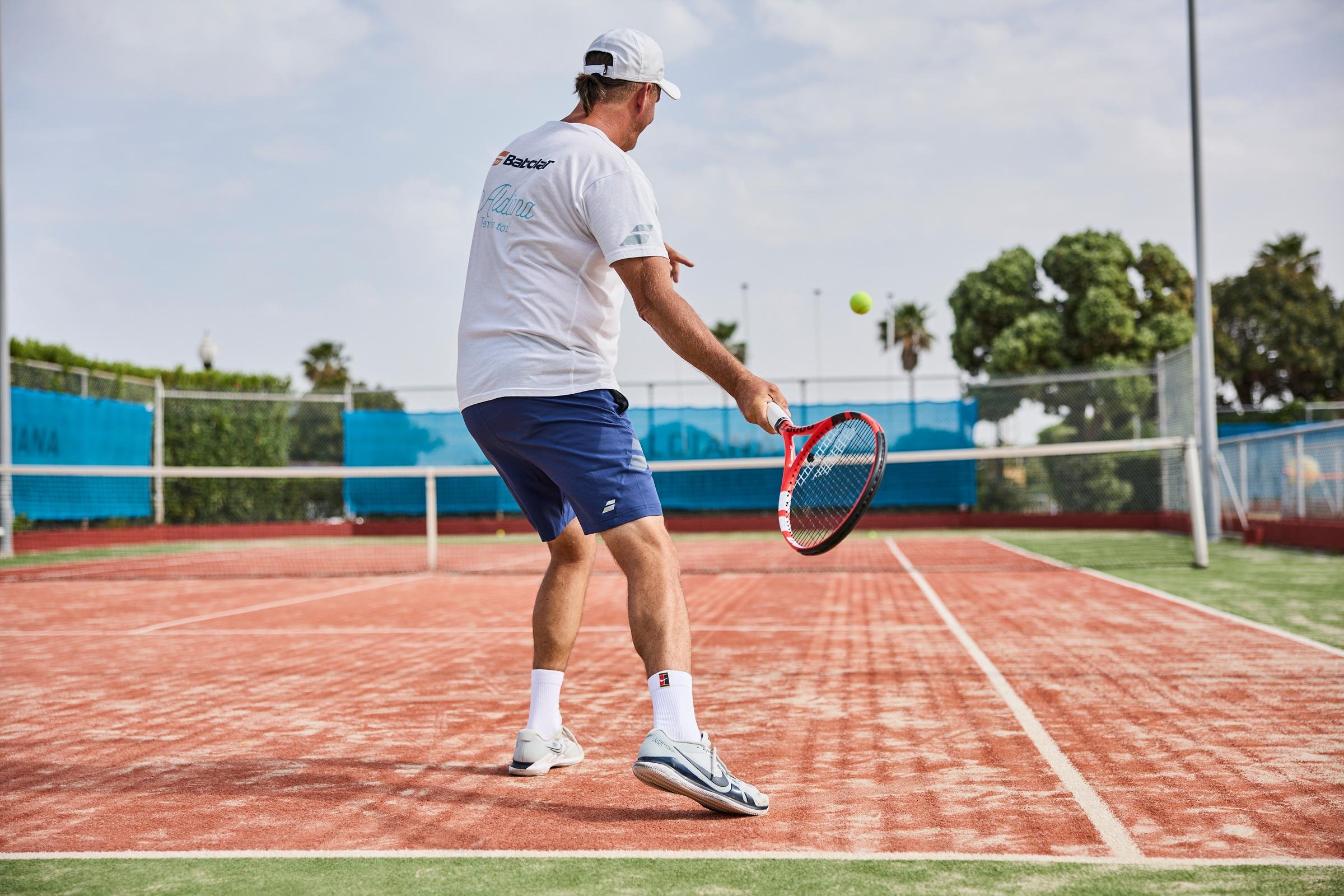Ein Mann spielt Tennis auf einem roten Platz im sonnigen Außenbereich