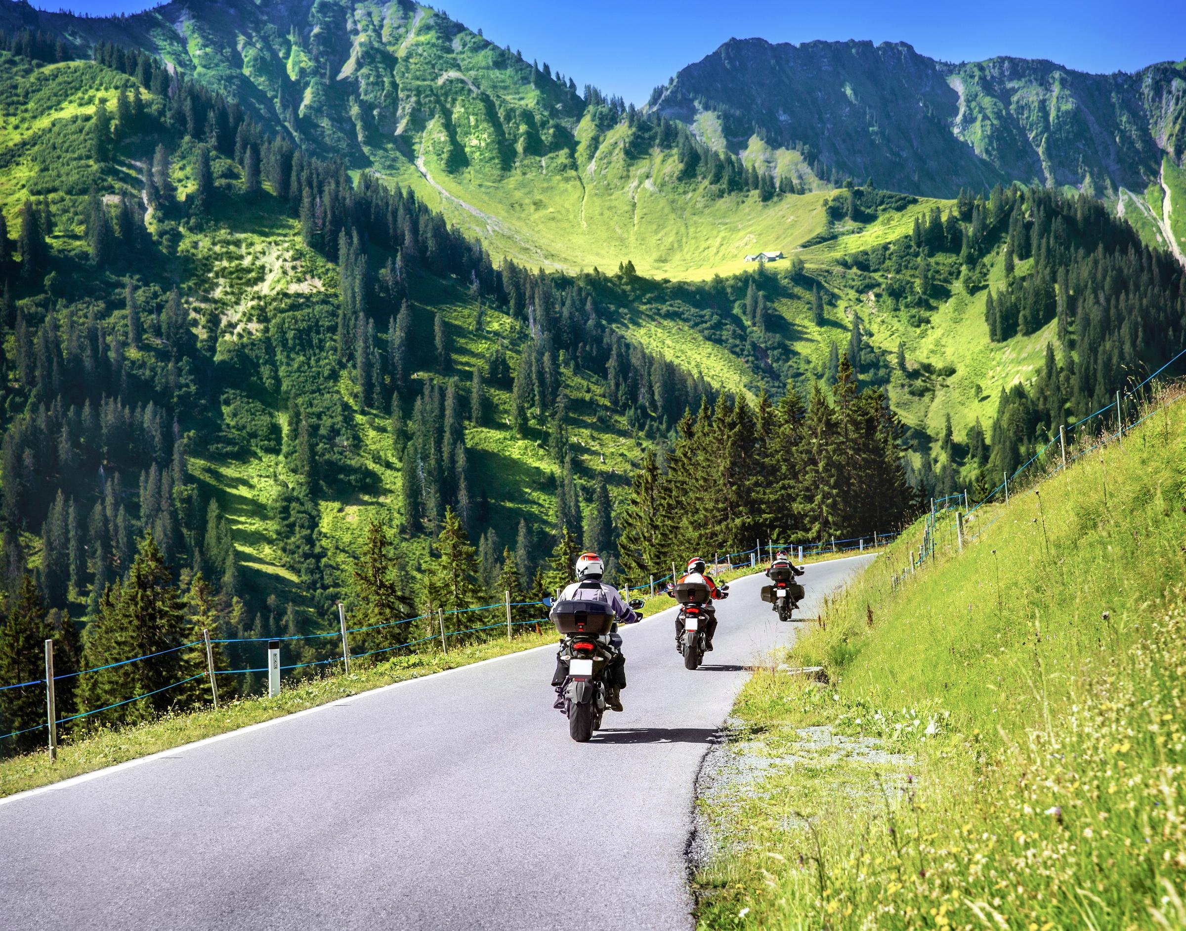 Biker fahren auf kurviger Straße durch grüne Berge bei strahlendem Himmel