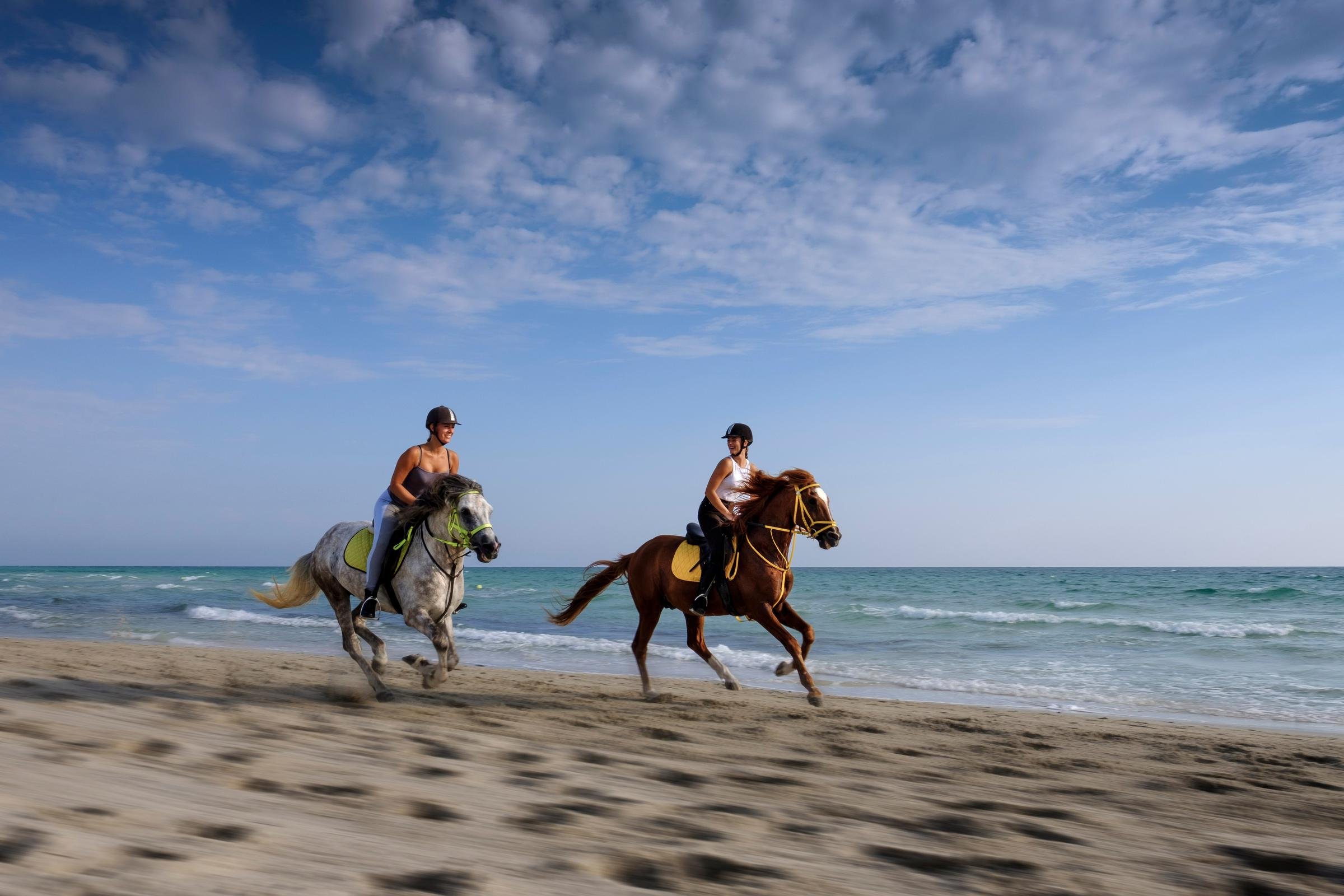 Zwei Personen reiten ganz nah am Meer entlang, erleben einen unvergesslichen Urlaub.
