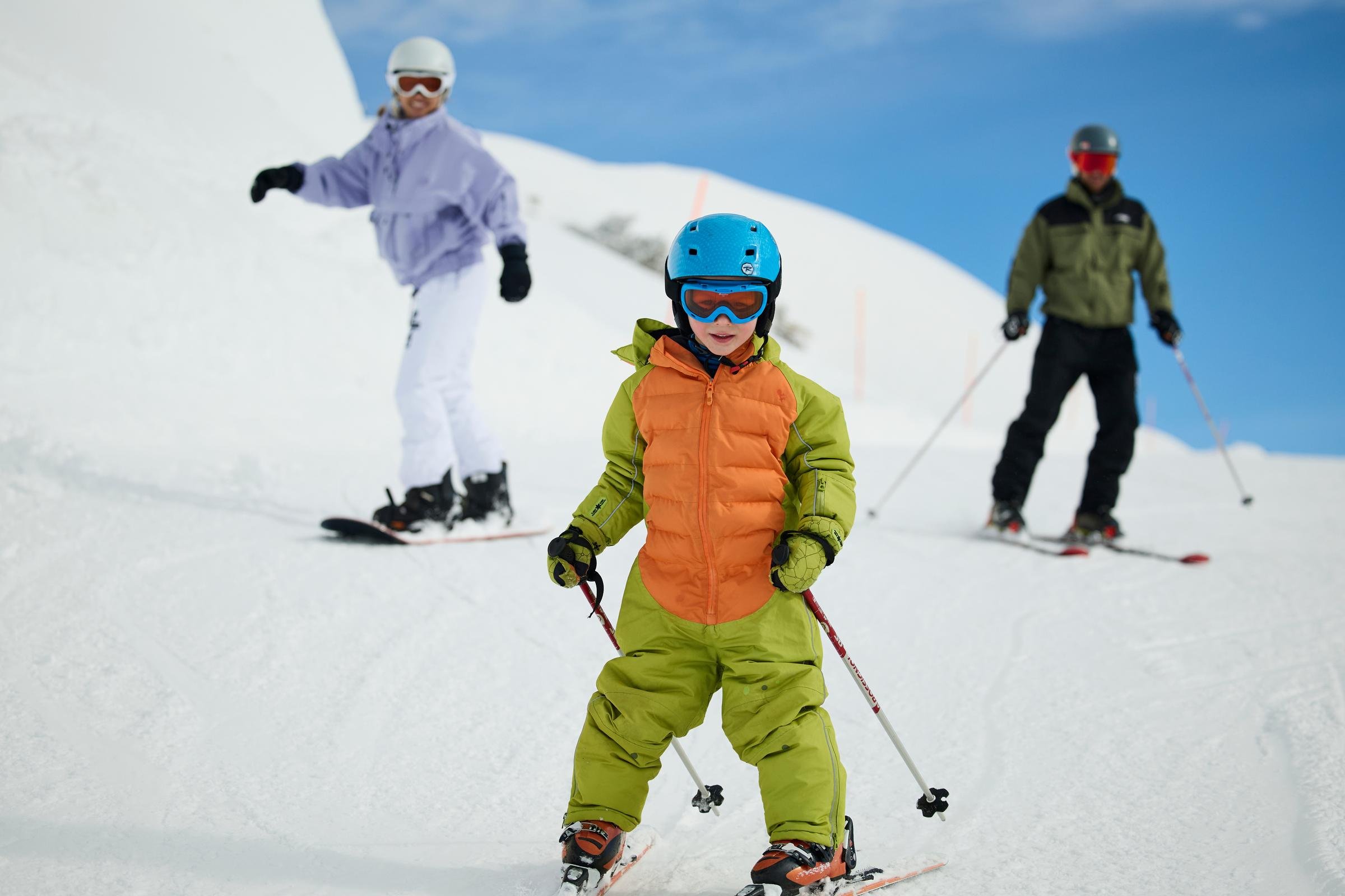 Drei Personen beim Skifahren auf verschneiten Bergen, eine mit blauer Schutzbrille und Helm