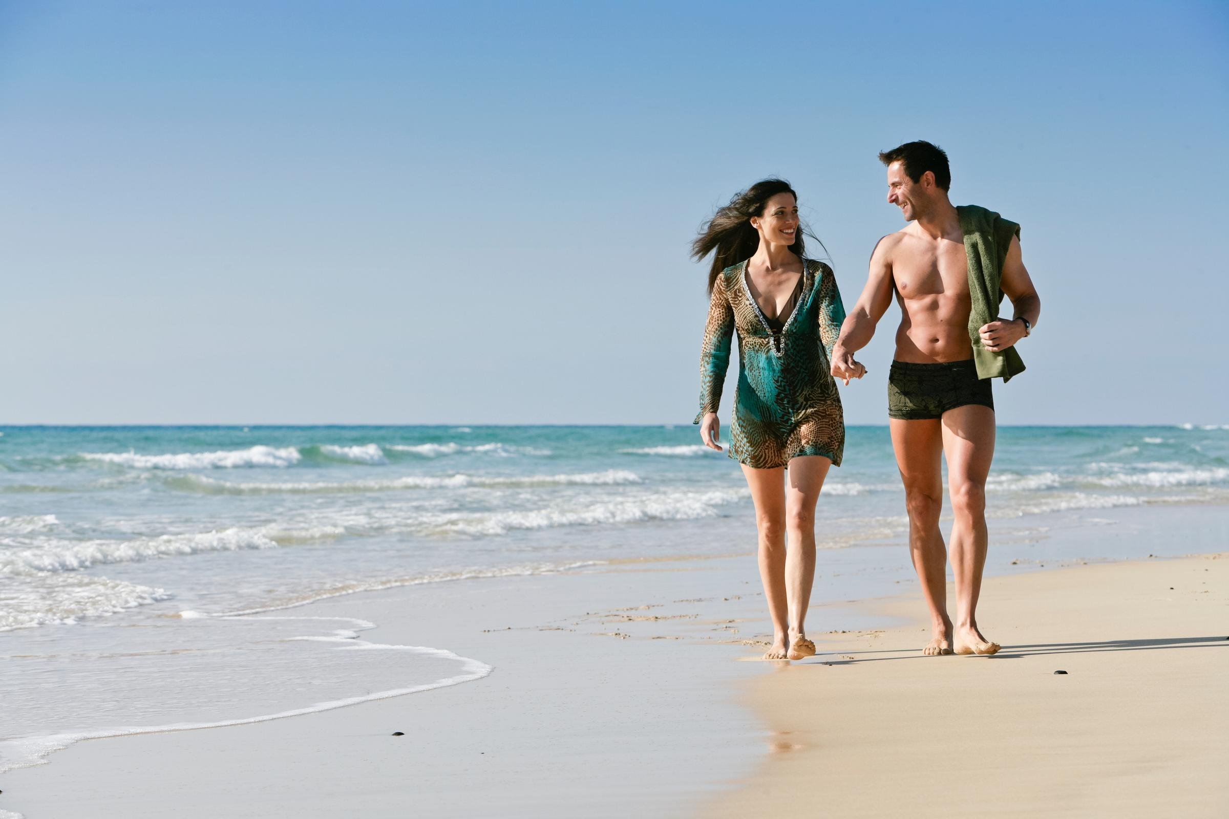 Zwei Menschen spazieren am Strand entlang, genießen einen Premium Cluburlaub bei Aldiana