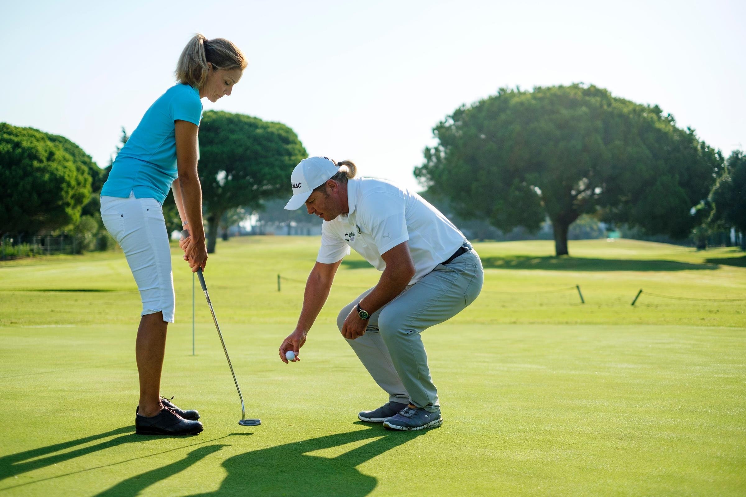 Ein Mann und eine Frau beim Golf auf einem gepflegten Rasen im Grünen, bei Sonnenschein