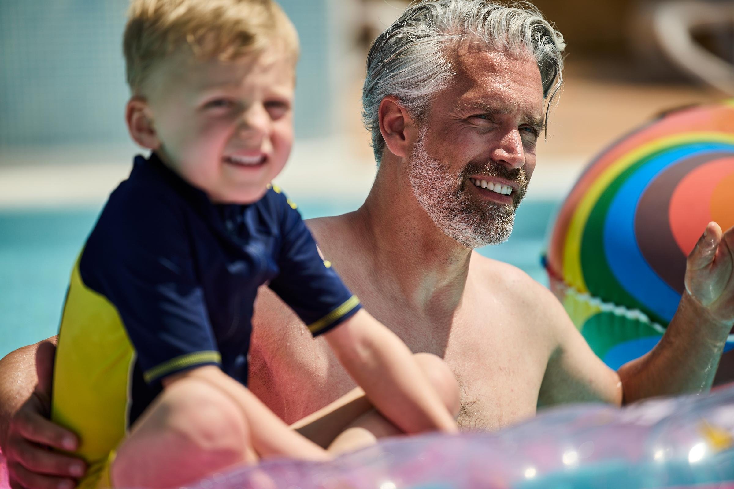 Ein älterer Mann mit einem Kind beim Spielen im Schwimmbad, idyllischer Urlaubs Moment