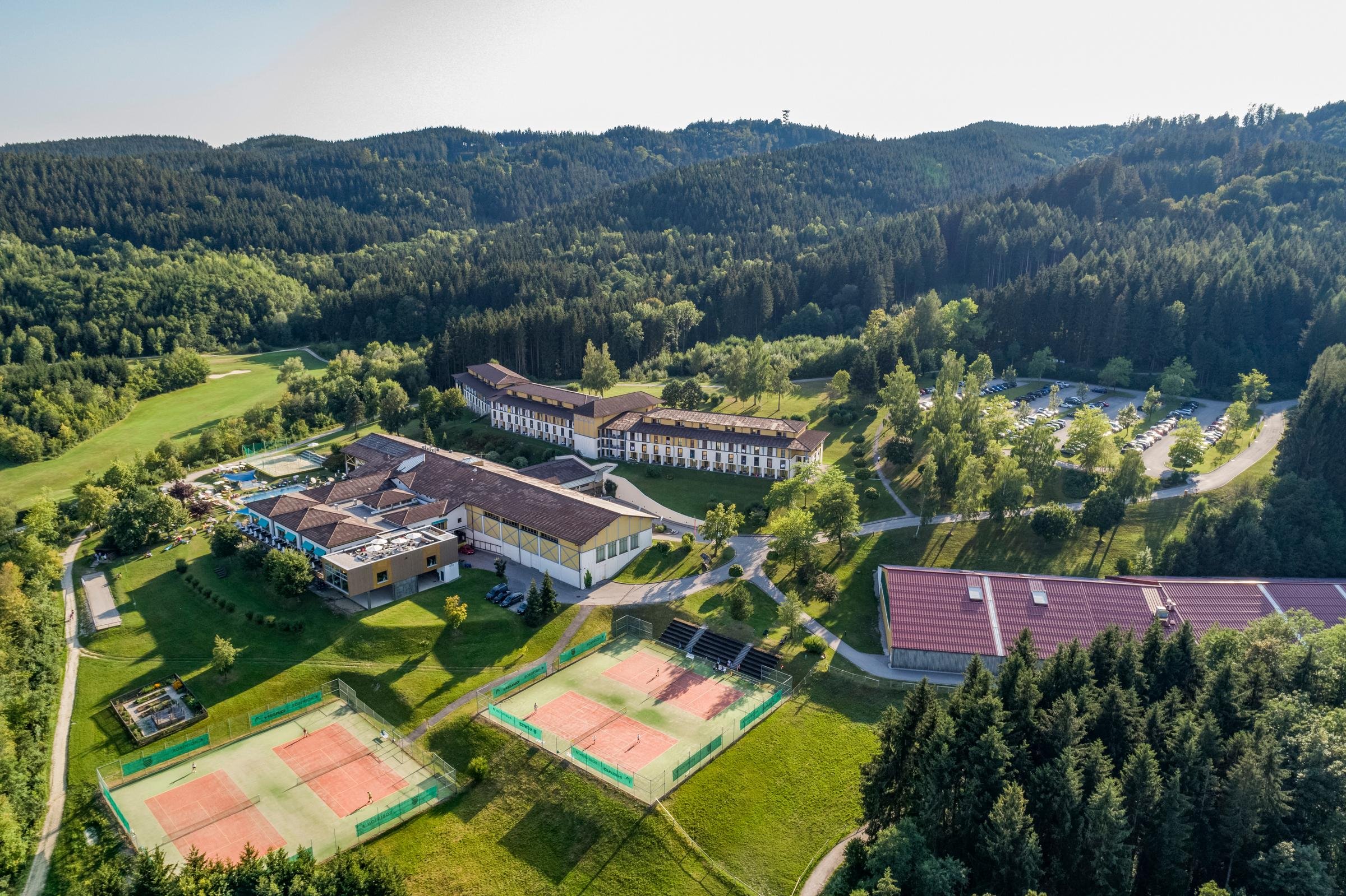 Eine Luftaufnahme des Aldiana Resorts inmitten grüner Berge mit Tennisplätzen und Sonnenschein