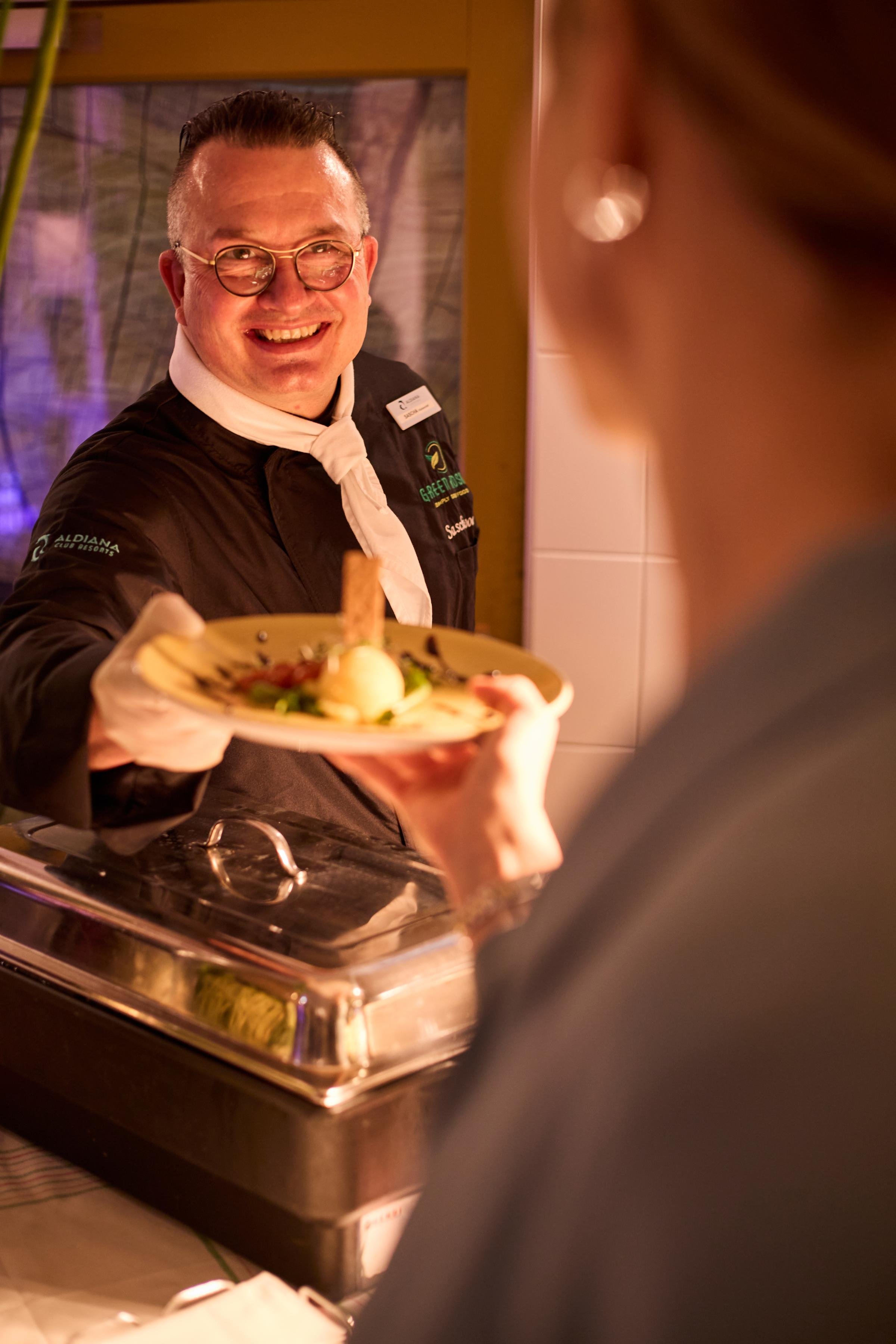 Ein Mitarbeiter im Premium Cluburlaub von Aldiana serviert ein Essen an einen Gast