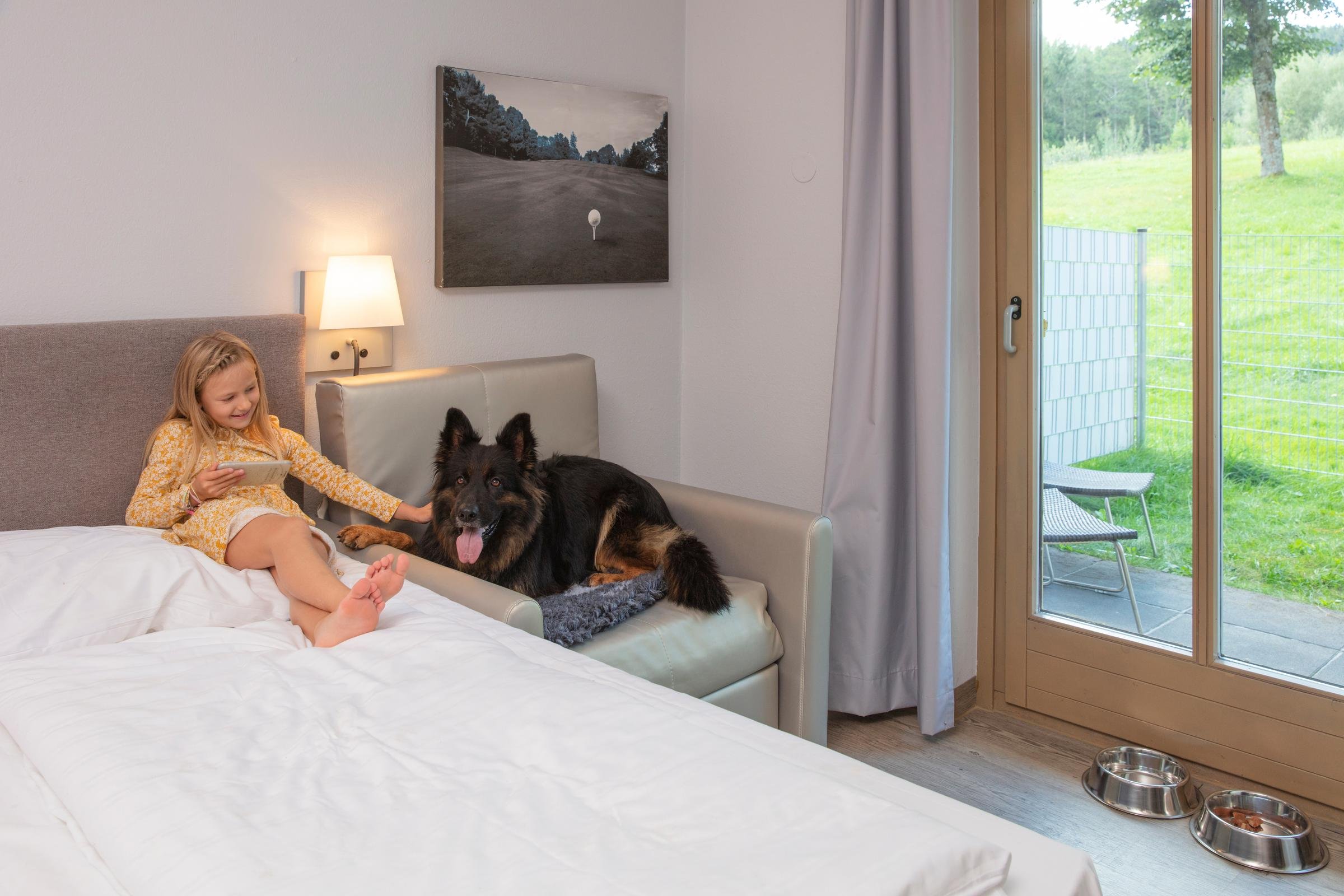 Jugendlicher und Hund auf Bett im hellen Schlafzimmer mit Balkonblick bei Aldiana Premium Cluburlaub