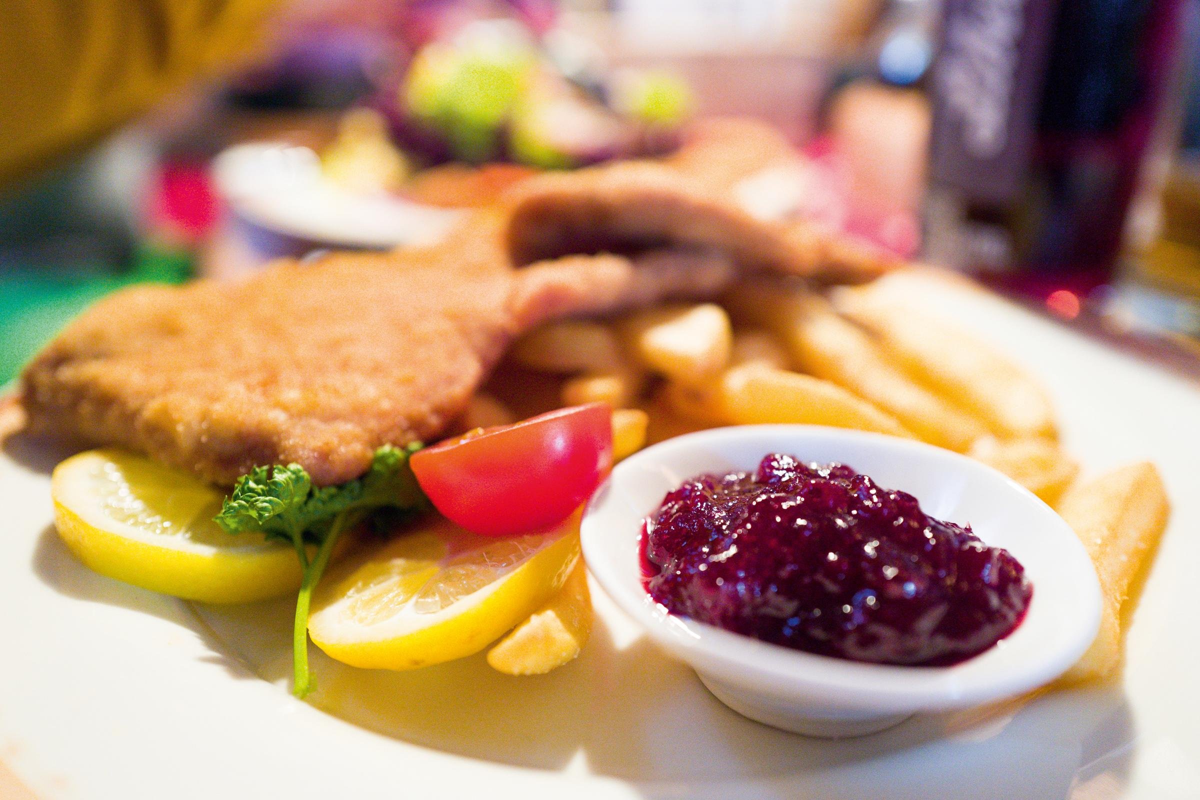 Gebratene Hähnchenflügel mit Zitronenscheiben, Petersilie und Himbeermarmelade auf weißem Teller