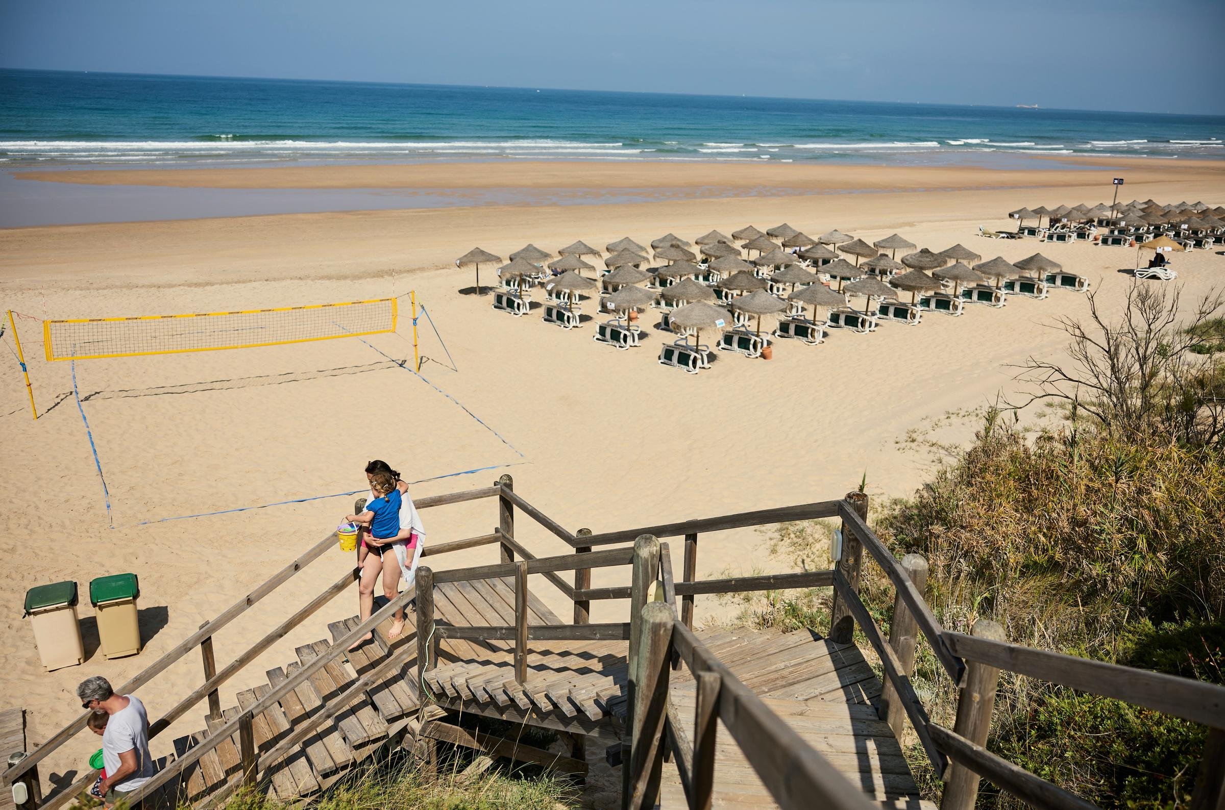 Strand mit Liegen und Sonnenschirmen, Treppen führen zum Sand, im Hintergrund das Meer