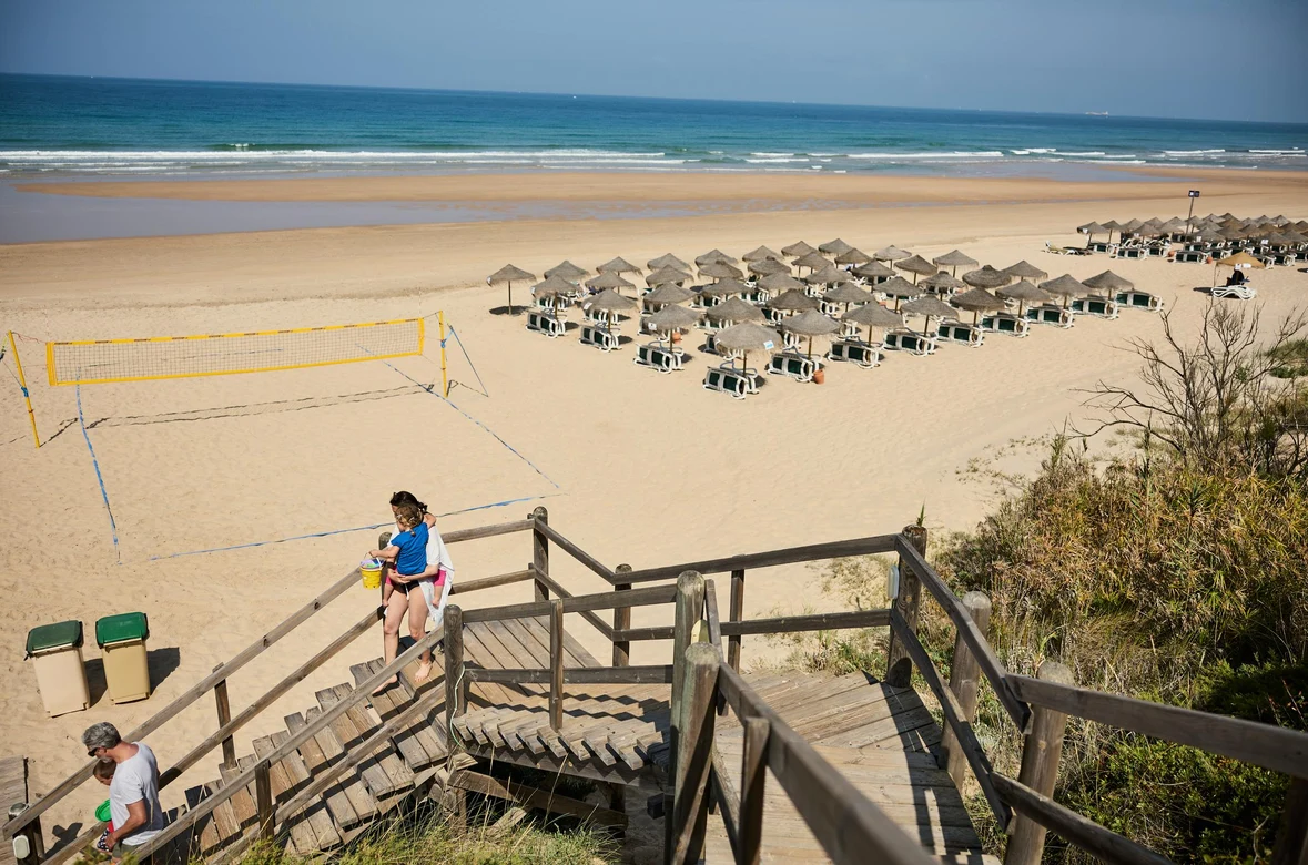 Strand mit Liegen und Sonnenschirmen, Treppen führen zum Sand, im Hintergrund das Meer