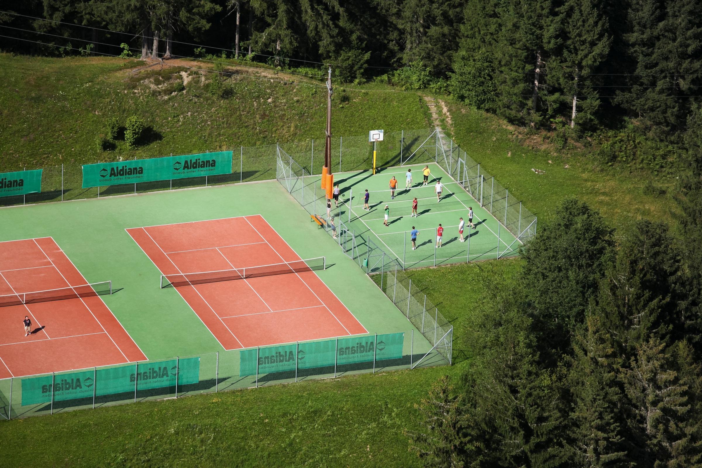 Detaillierte Ansicht eines Tennisplatzes bei Aldiana mit Spielern im Spiel, umgeben von Natur.