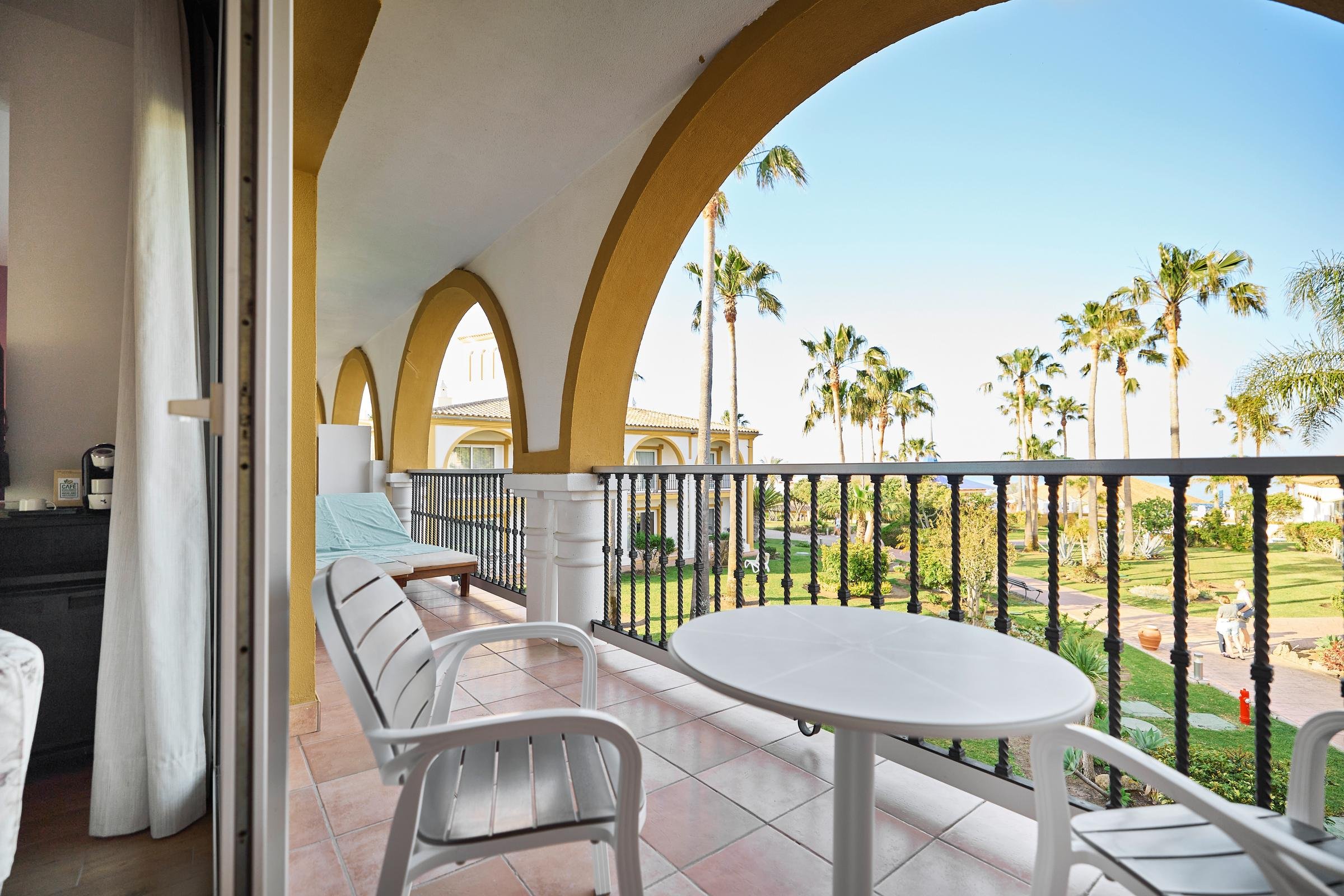 Blick auf eine balkonartige Terrasse mit Tischen, Stühlen und Palmbaum im Urlaubsort
