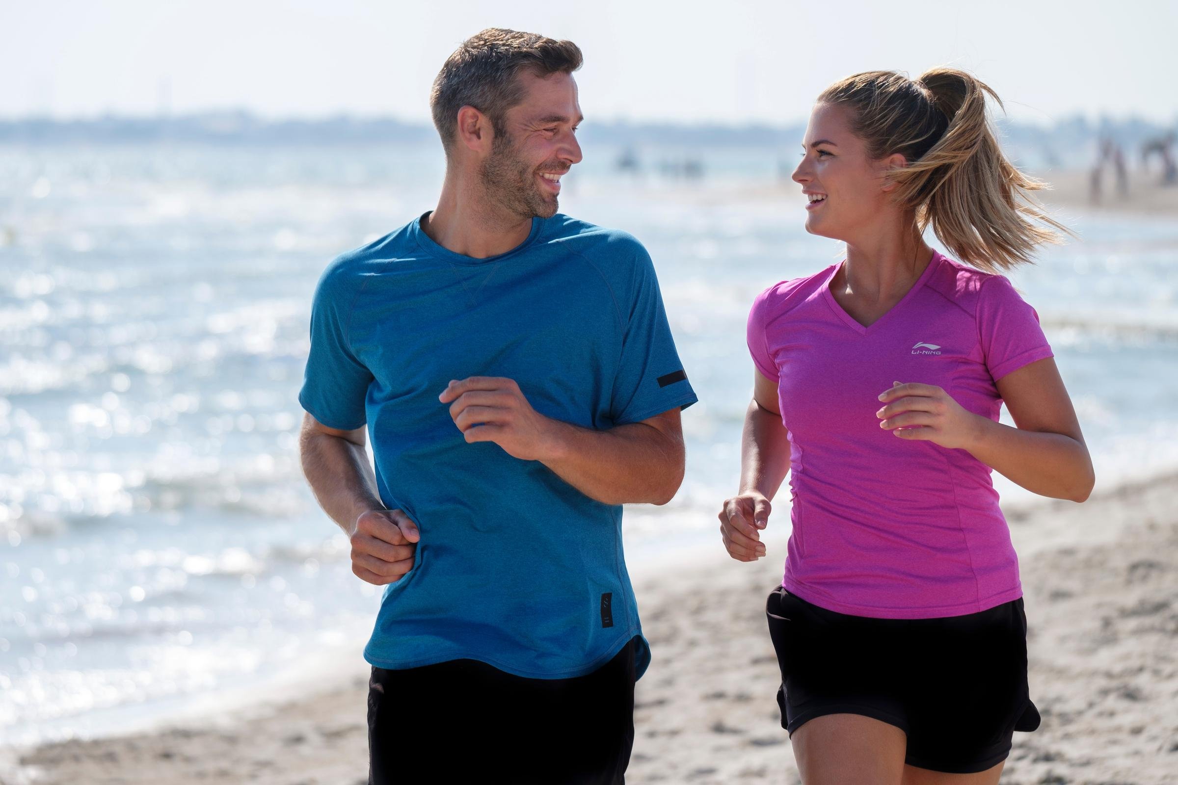 Zwei Jogger laufen am Strand entlang entlang der Küste bei Sonnenwetter, sportlich unterwegs
