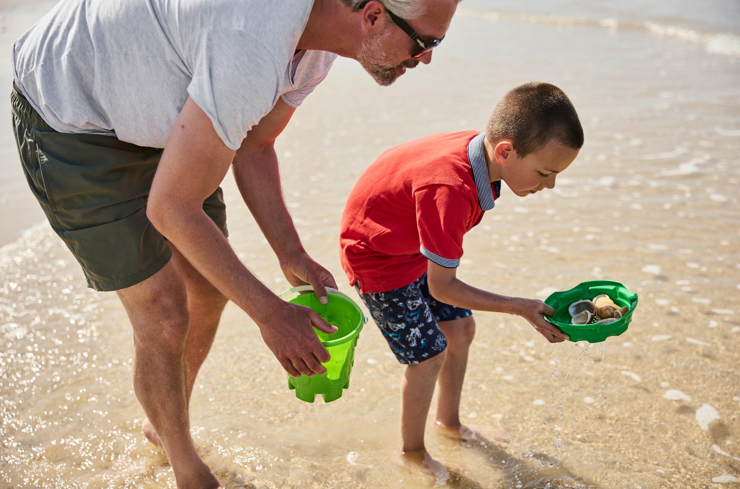 Zwei Erwachsene und Kind beim Sandspielen am Strand mit Spielsachen, fröhlicher Ausflug