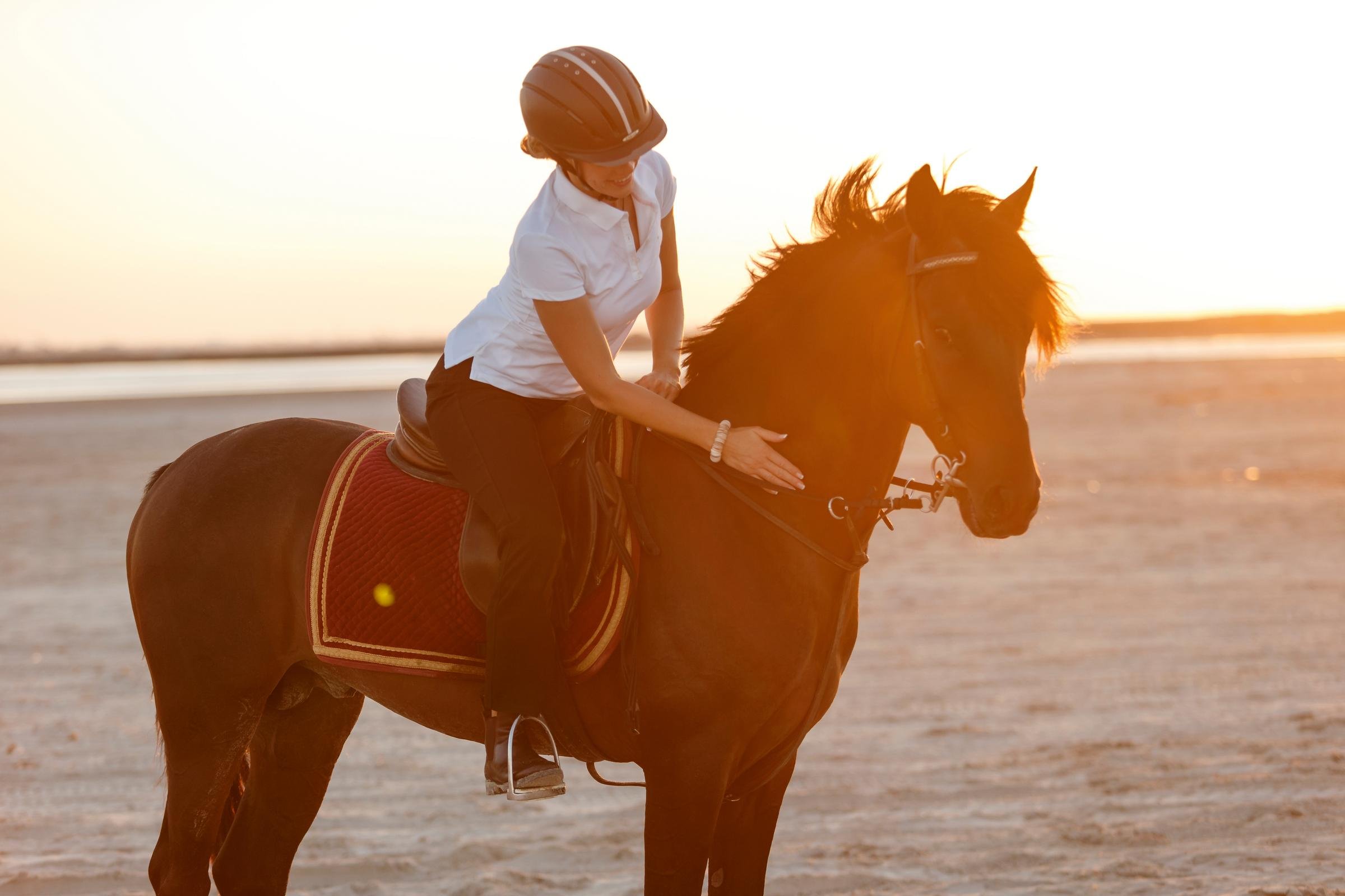 Frau reitet auf einem Pferd am Strand bei Sonnenuntergang, entspannt und elegant.