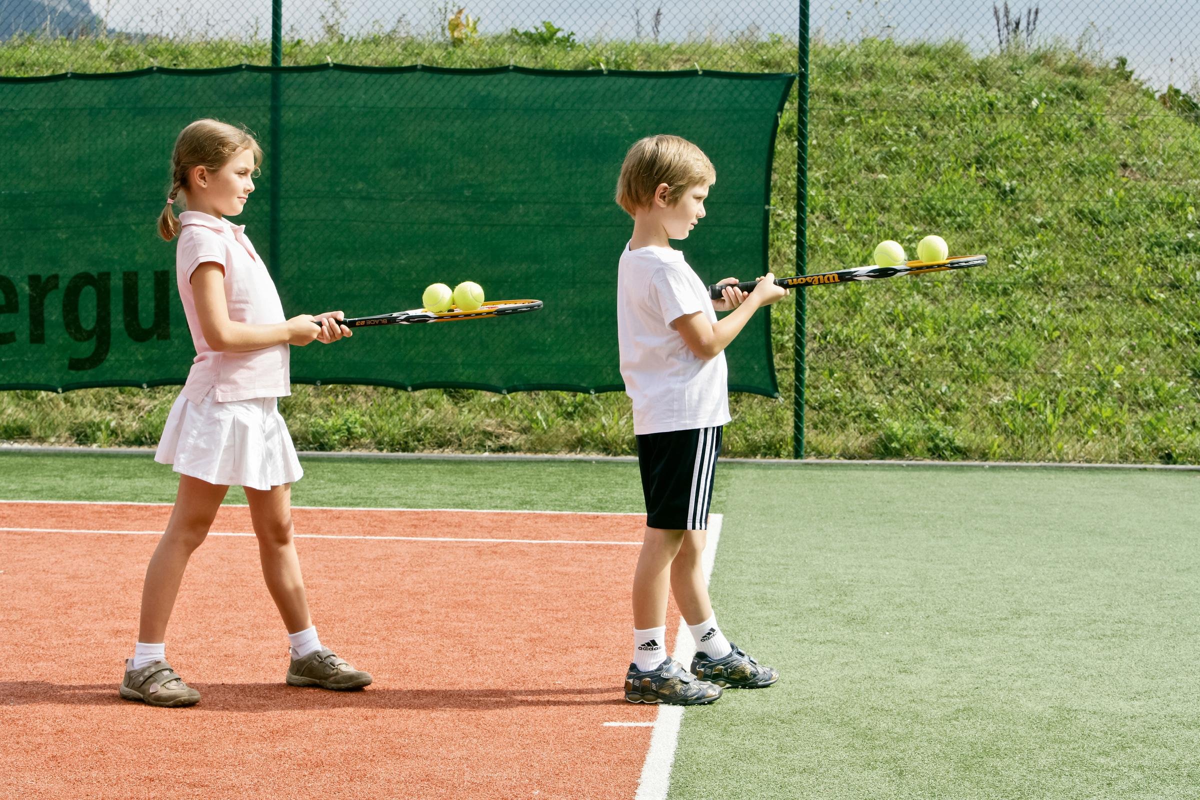 Zwei Kinder mit Tennisbällen auf einem Tennisplatz beim Üben, ideal für einen Premium Cluburlaub
