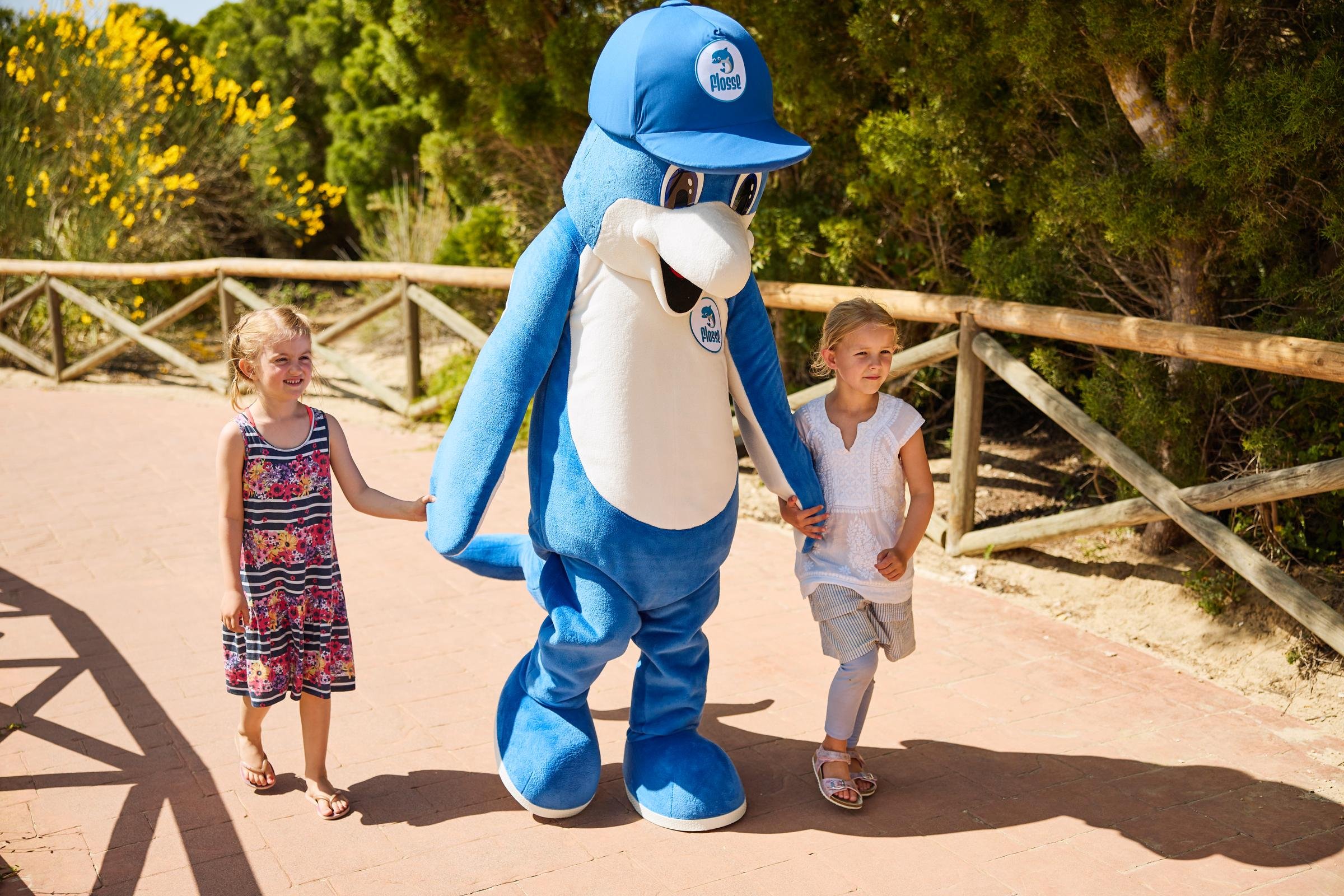 Kindermaskottchen von Aldiana läuft mit zwei Kindern auf einem Weg im Freien
