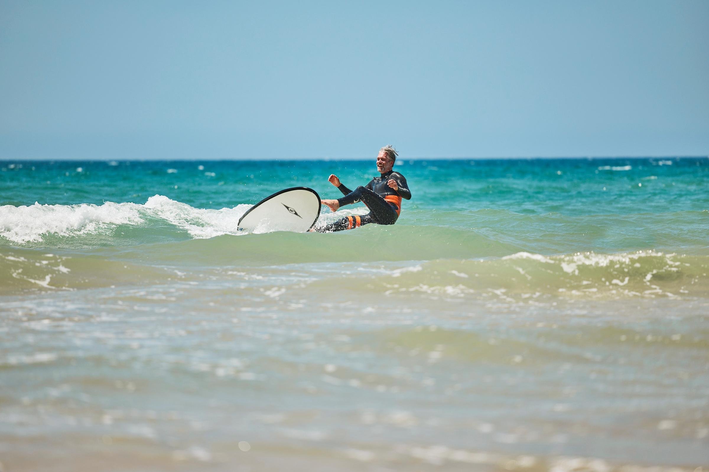 Ein Surfer im Meer, im Hintergrund blauer Himmel, Sandstrand, Urlaub bei Aldiana