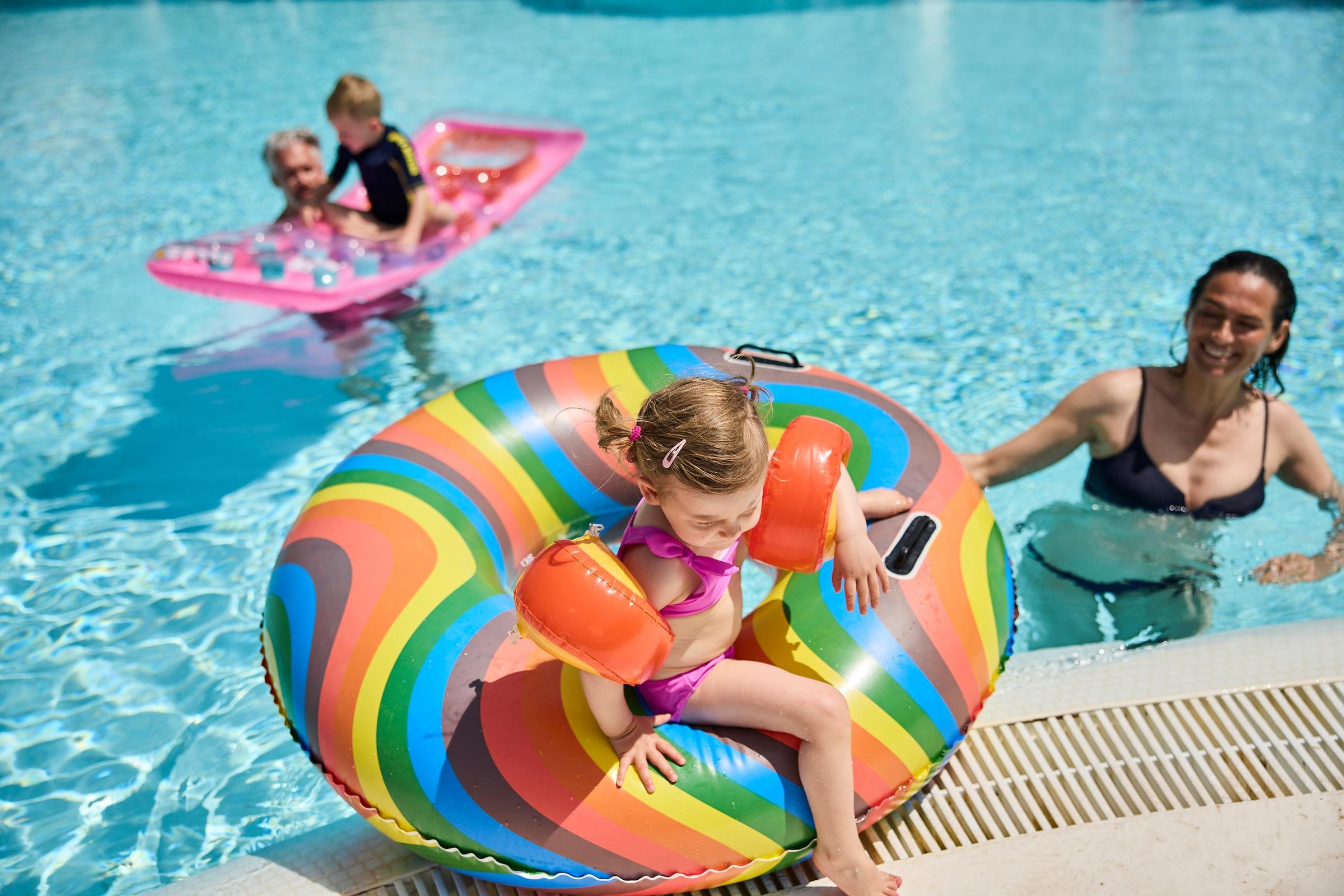 Kinder auf einer bunten Poolmatte und einer weiteren Person im Pool in einem hochwertigen Cluburlaubsambiente