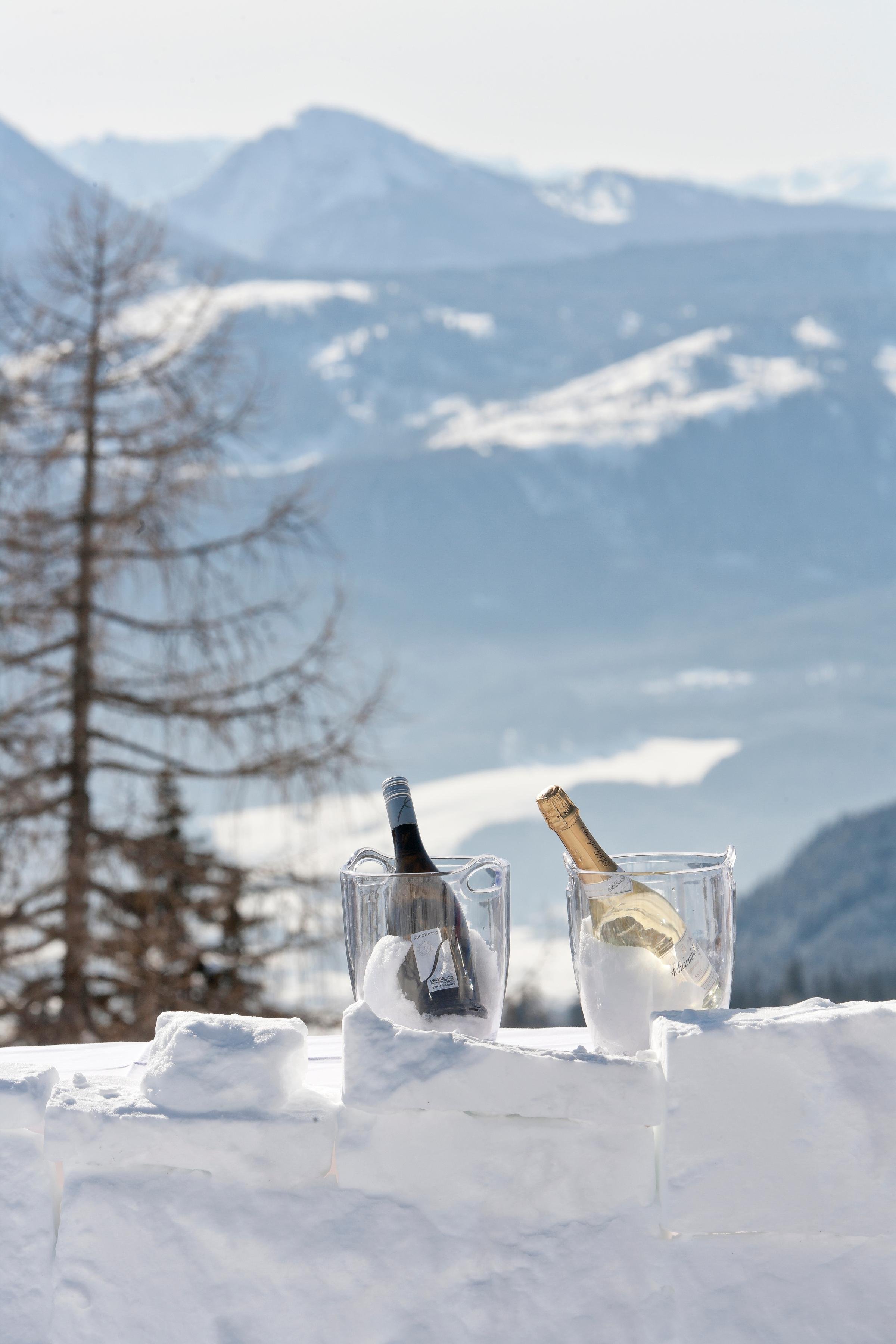 Ein winterliches Landschaftsbild mit Schnee, Bergen und zwei Gläser mit Wein im Schnee