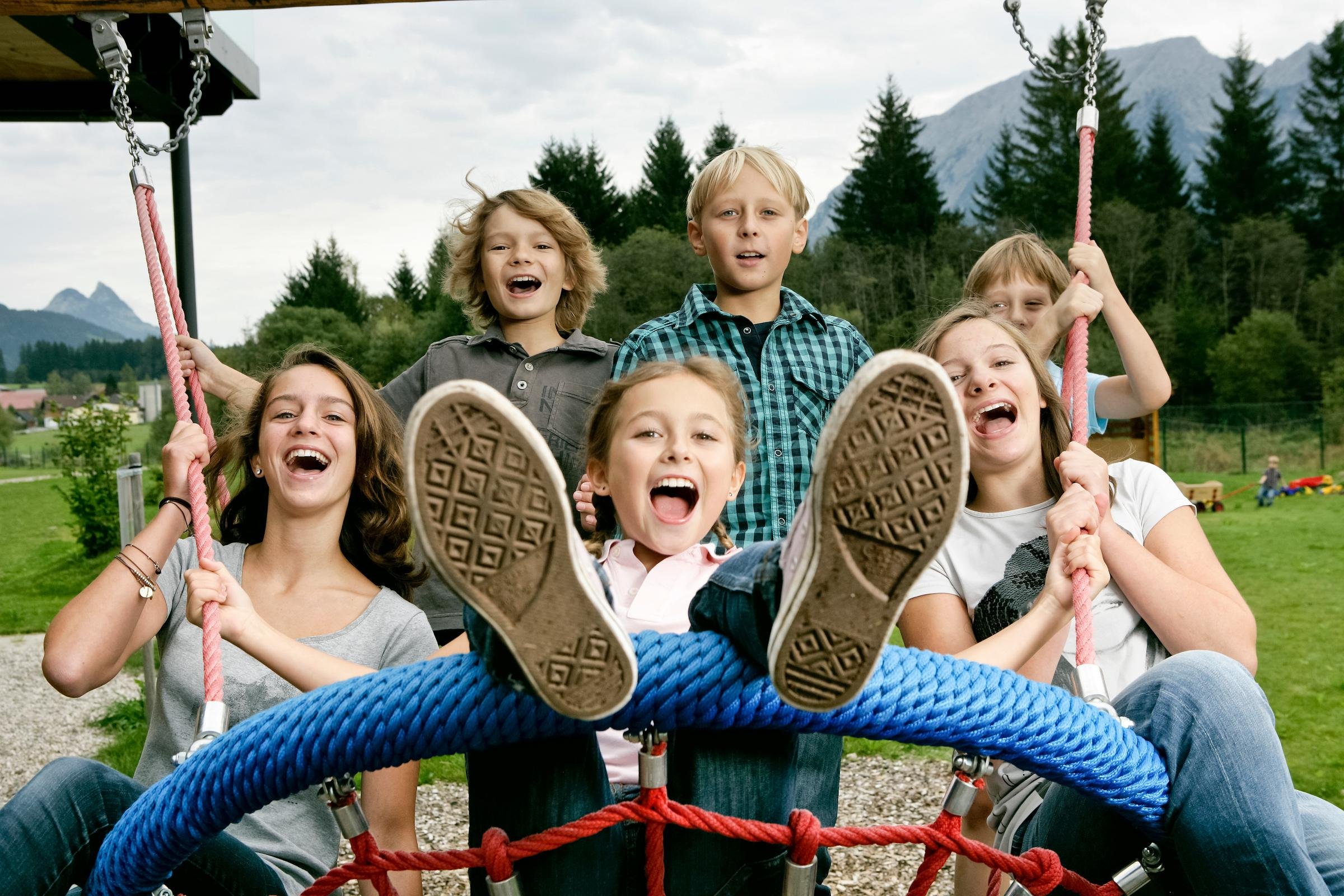 Eine Gruppe von Menschen sitzt auf einer Schaukel im grünen Park bei Aldiana, entspannt und lachend