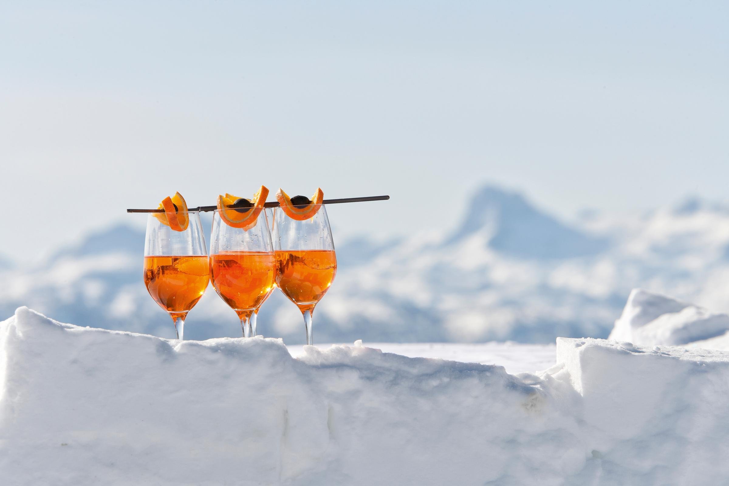 Elegantes Getränk in 3 Weingläsern auf Schneelandschaft bei Sonnenlicht, hochwertige Urlaubsatmosphäre