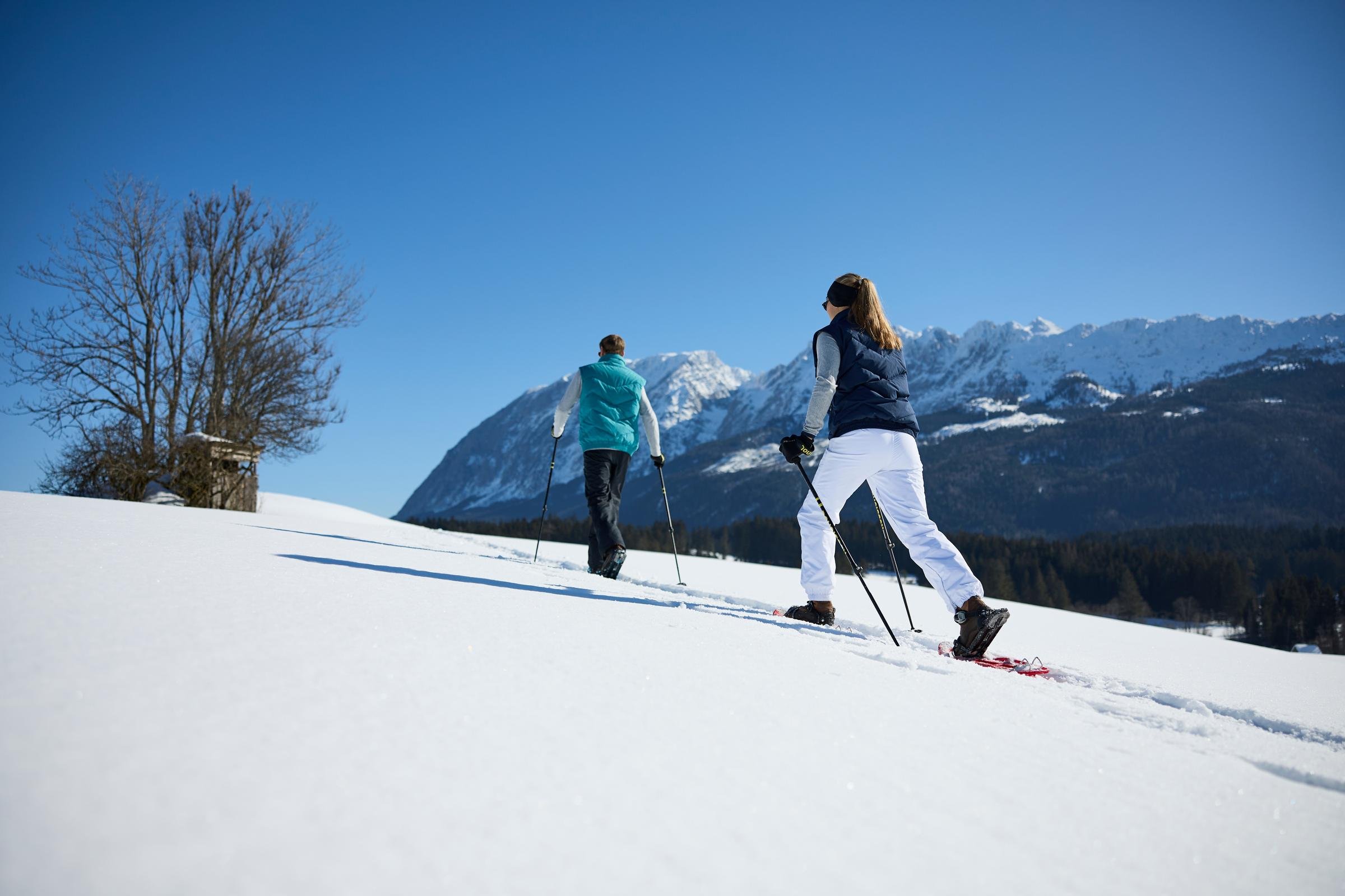 Zwei Skifahrer auf verschneiter Piste vor beeindruckenden Berggipfeln, sonniger Wintertag