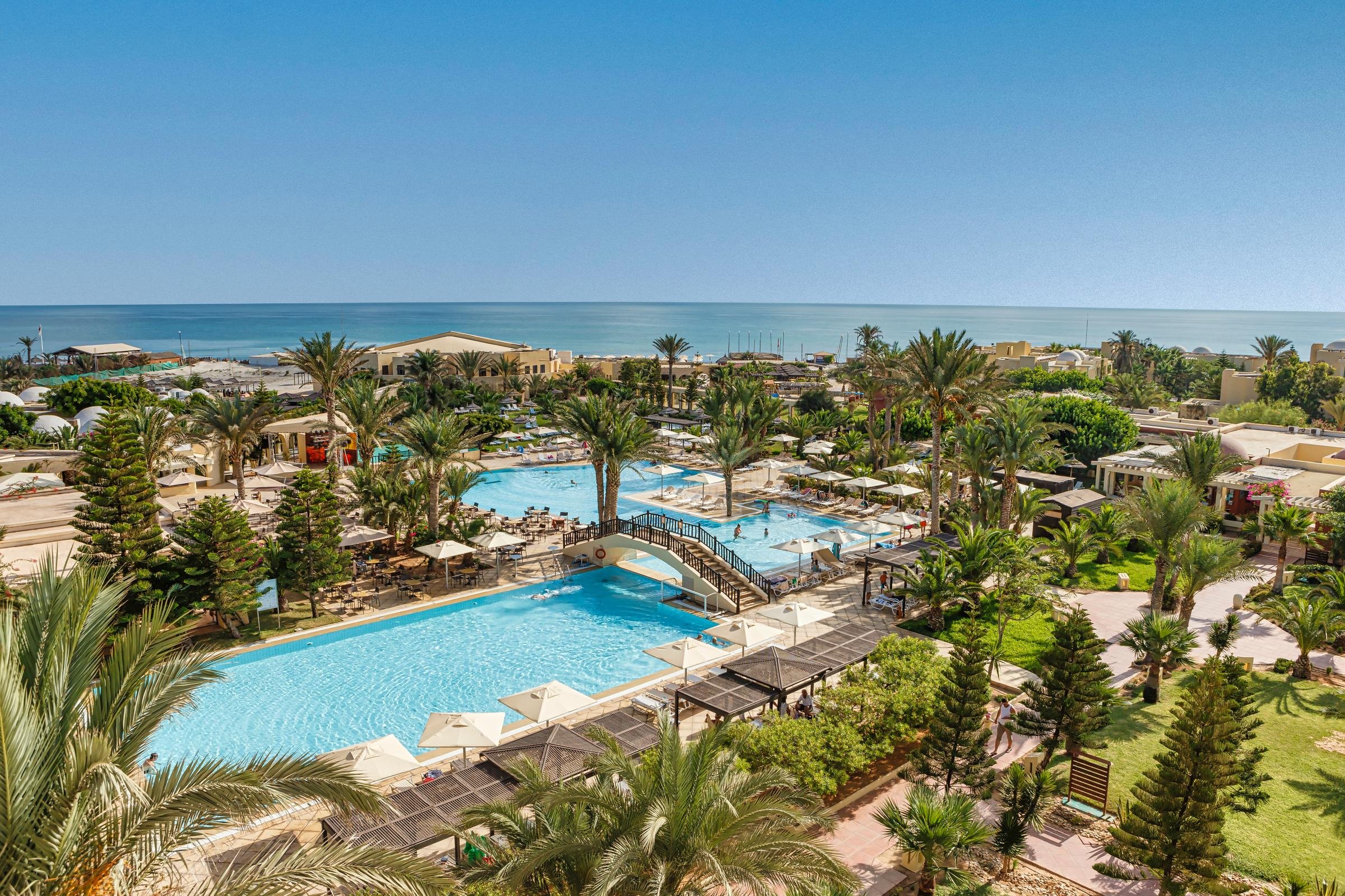 Blick auf den luxuriösen Hotelpoolbereich bei Aldiana mit Palmen und Meer im Hintergrund
