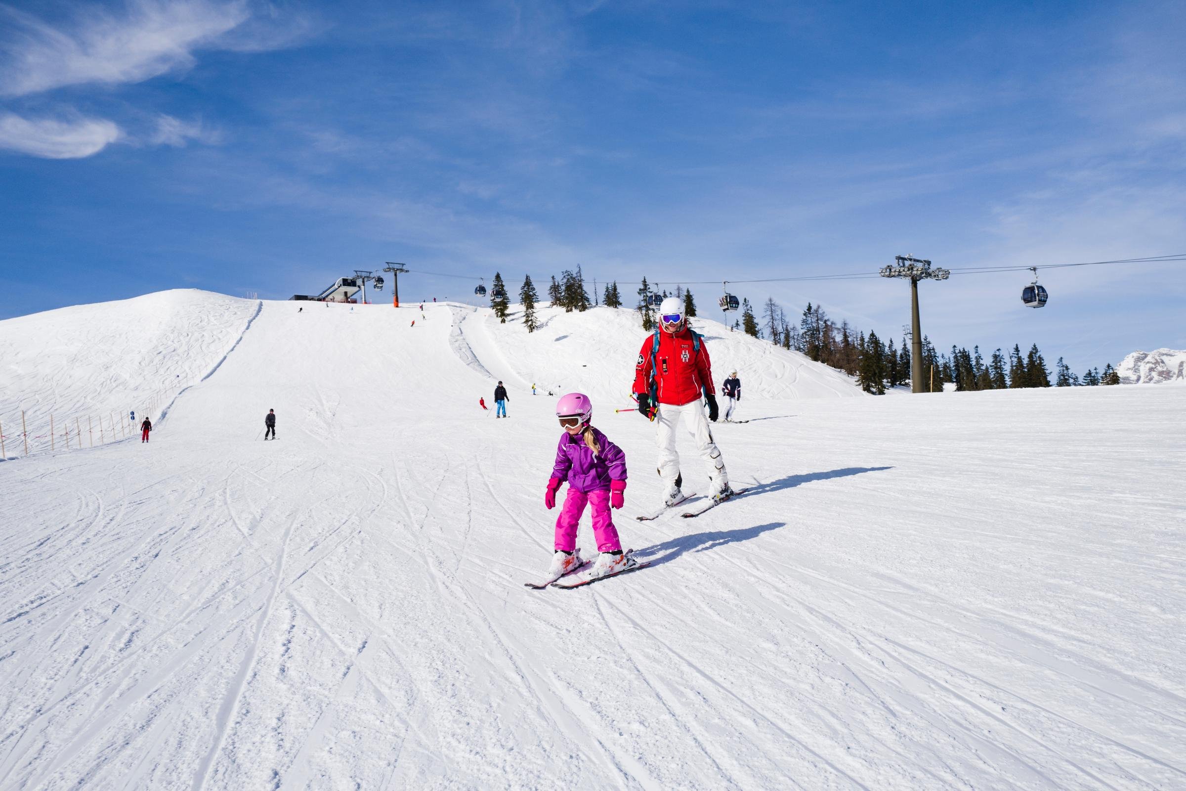 Familie beim Skifahren auf schneebedeckter Piste mit Bergpanorama bei Sonnenschein