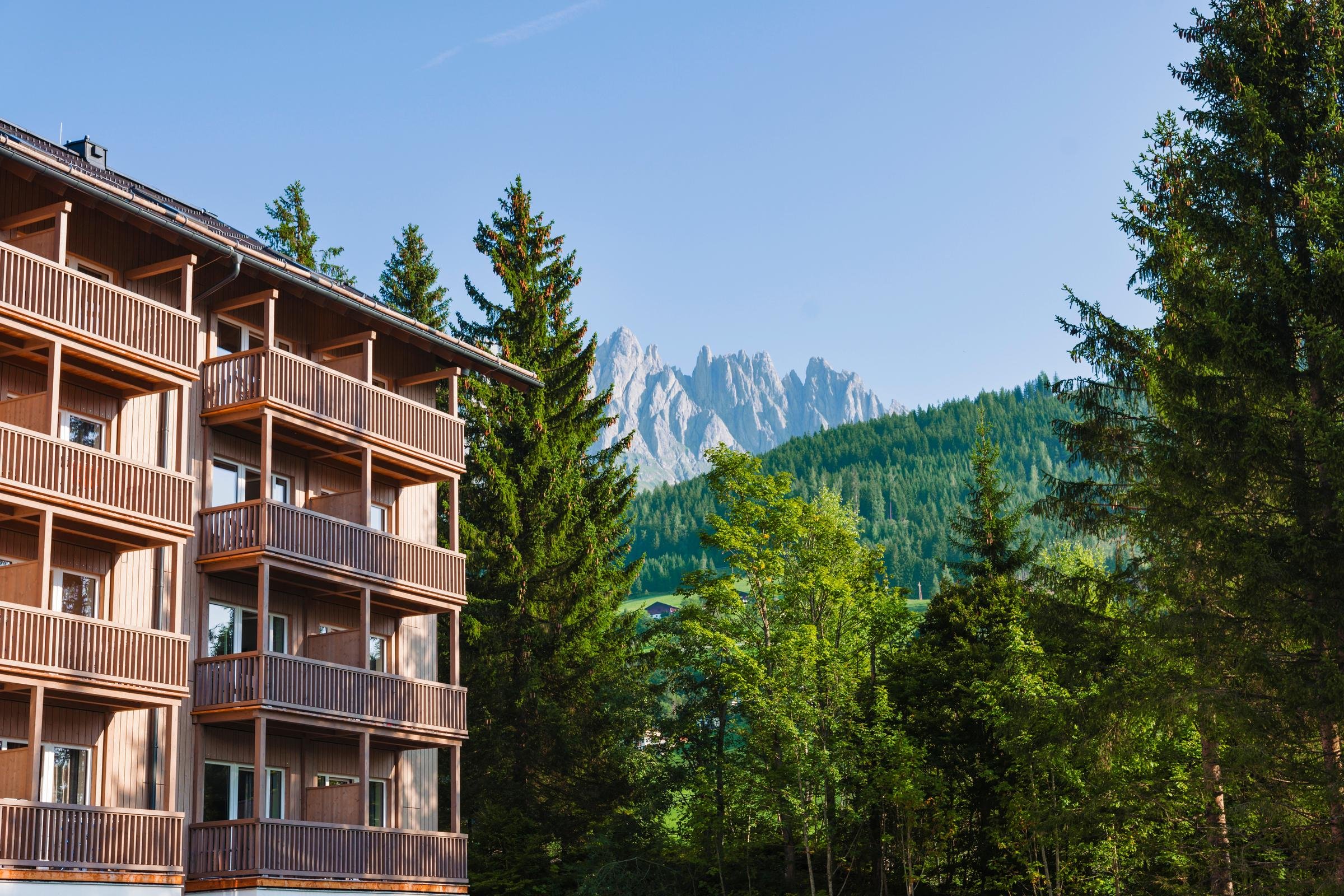 Mehrstöckiges Hotelgebäude in den Bergen, umgeben von Wald, bei Sonnenlicht, im Urlaub.