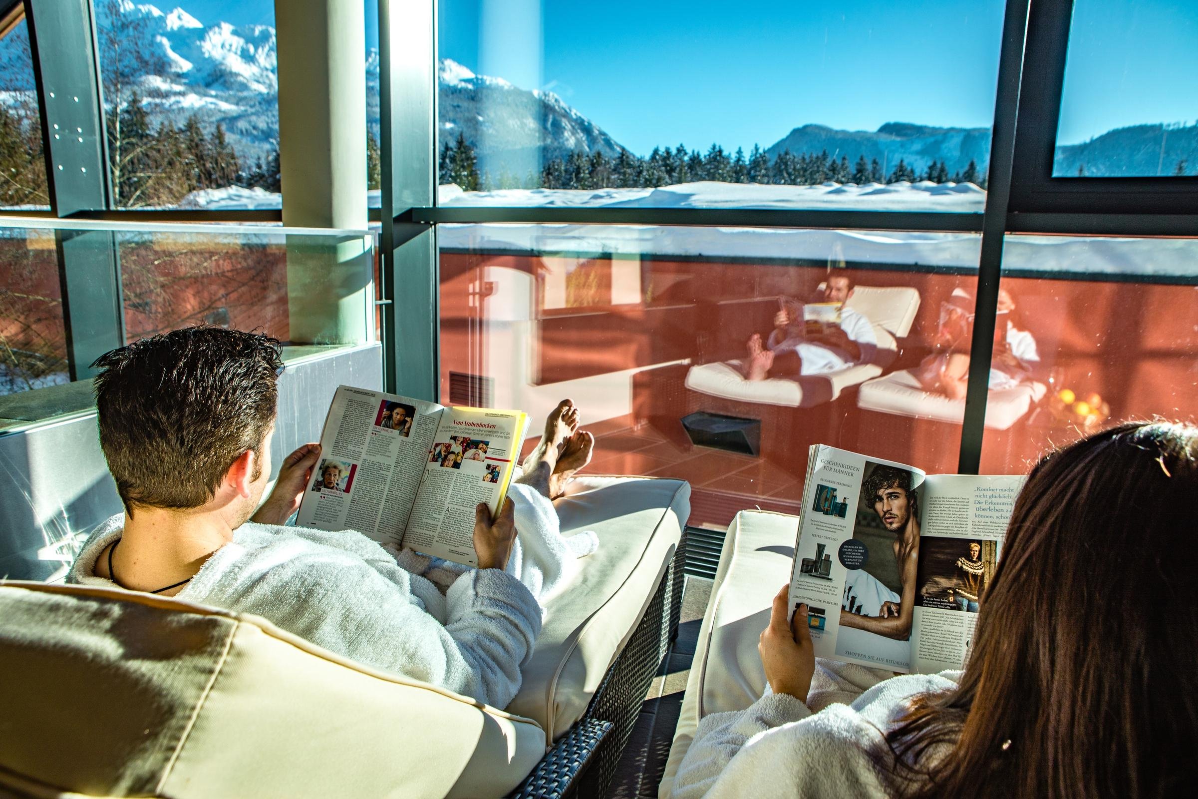 Zwei Personen lesen im Luftfahrzeug mit Blick auf die Alpen, entspannter Premium Cluburlaub