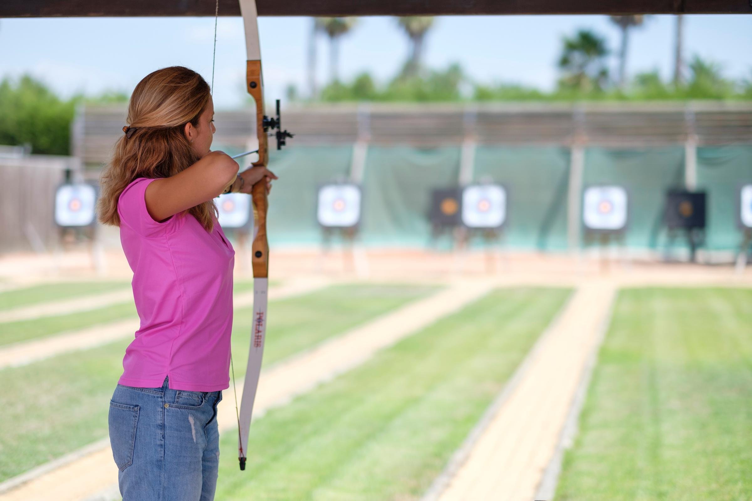 Frau beim Bogenschießen auf einer gepflegten, grünen Außenanlage bei Aldiana.
