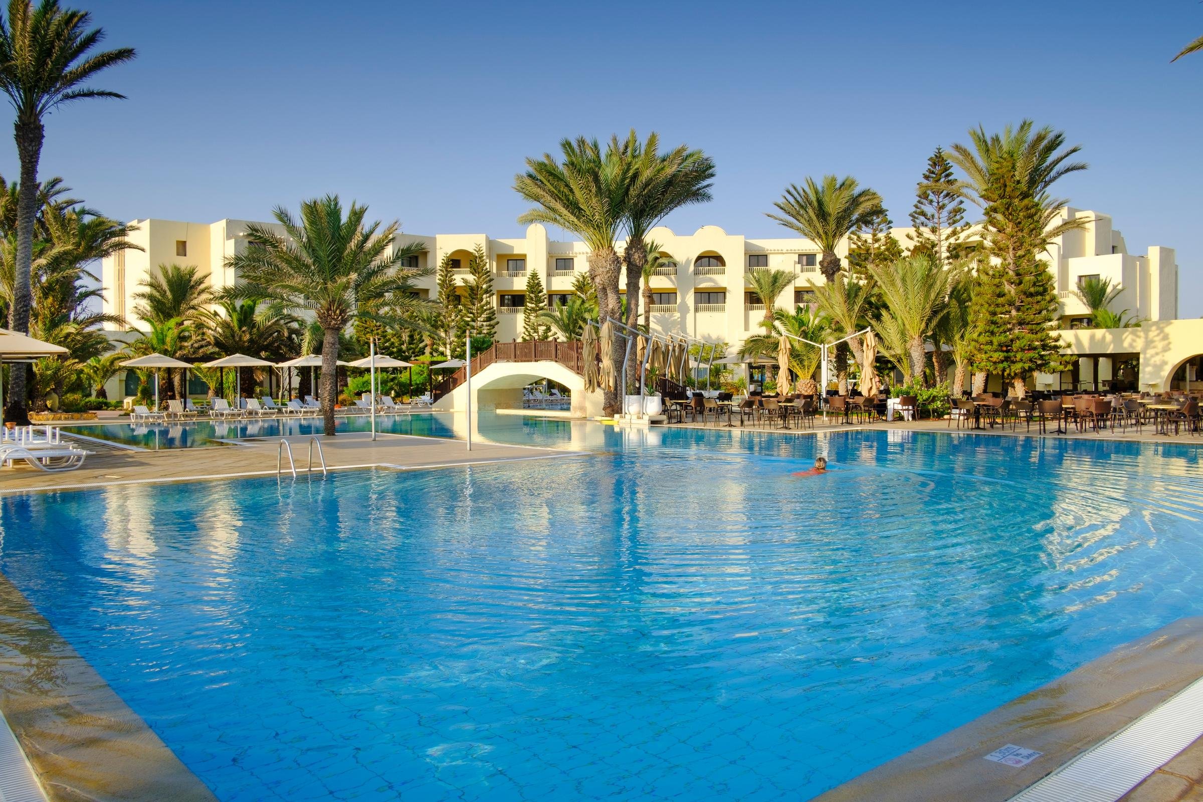 Blick auf einen luxuriösen Poolbereich bei Aldiana mit Palmen und Sonnenschirmen, Premium Cluburlaub