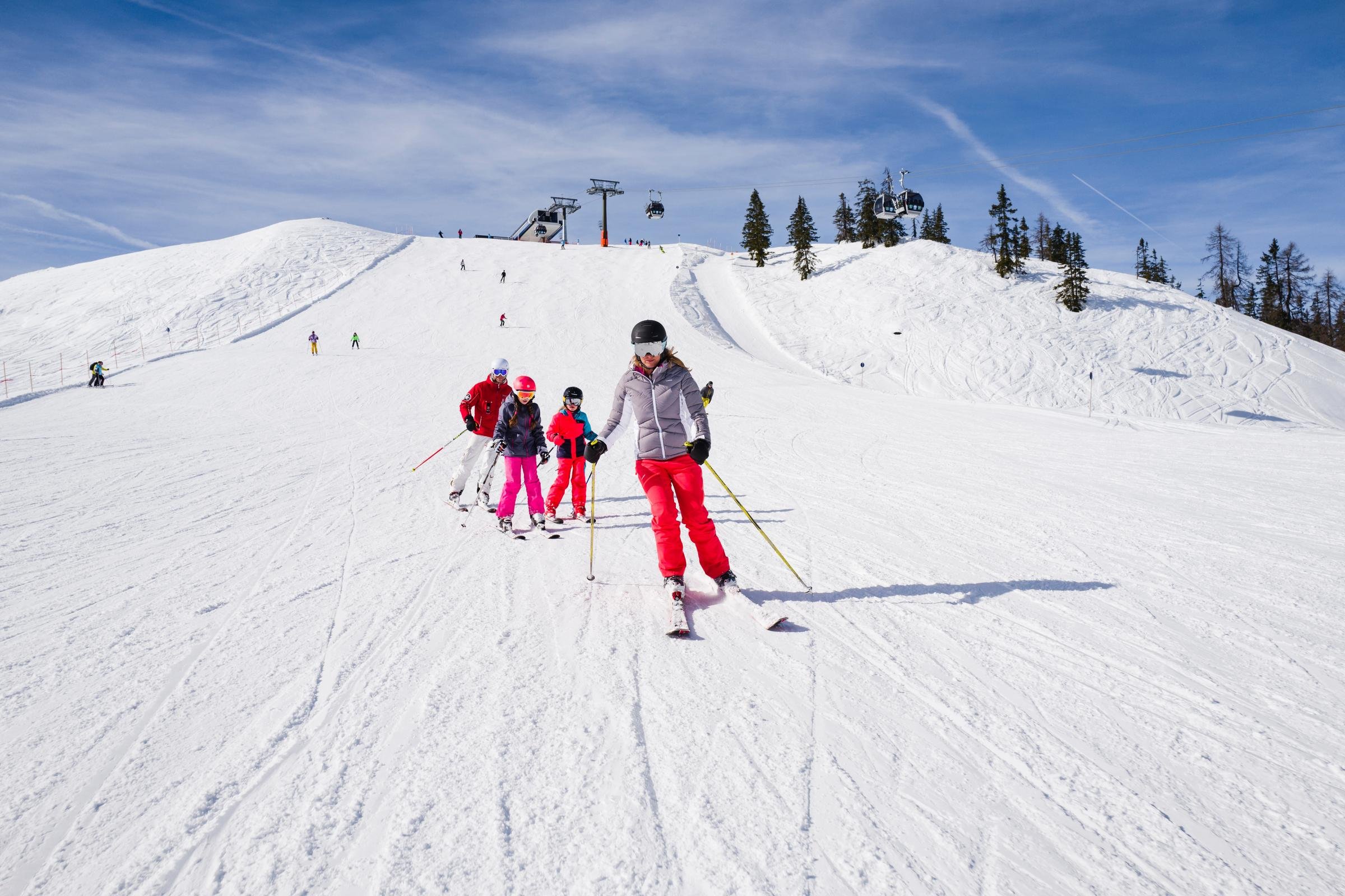 Schneeschuhläufer auf einem verschneiten Berg bei Sonnenlicht, klare Himmel, Bäume im Hintergrund