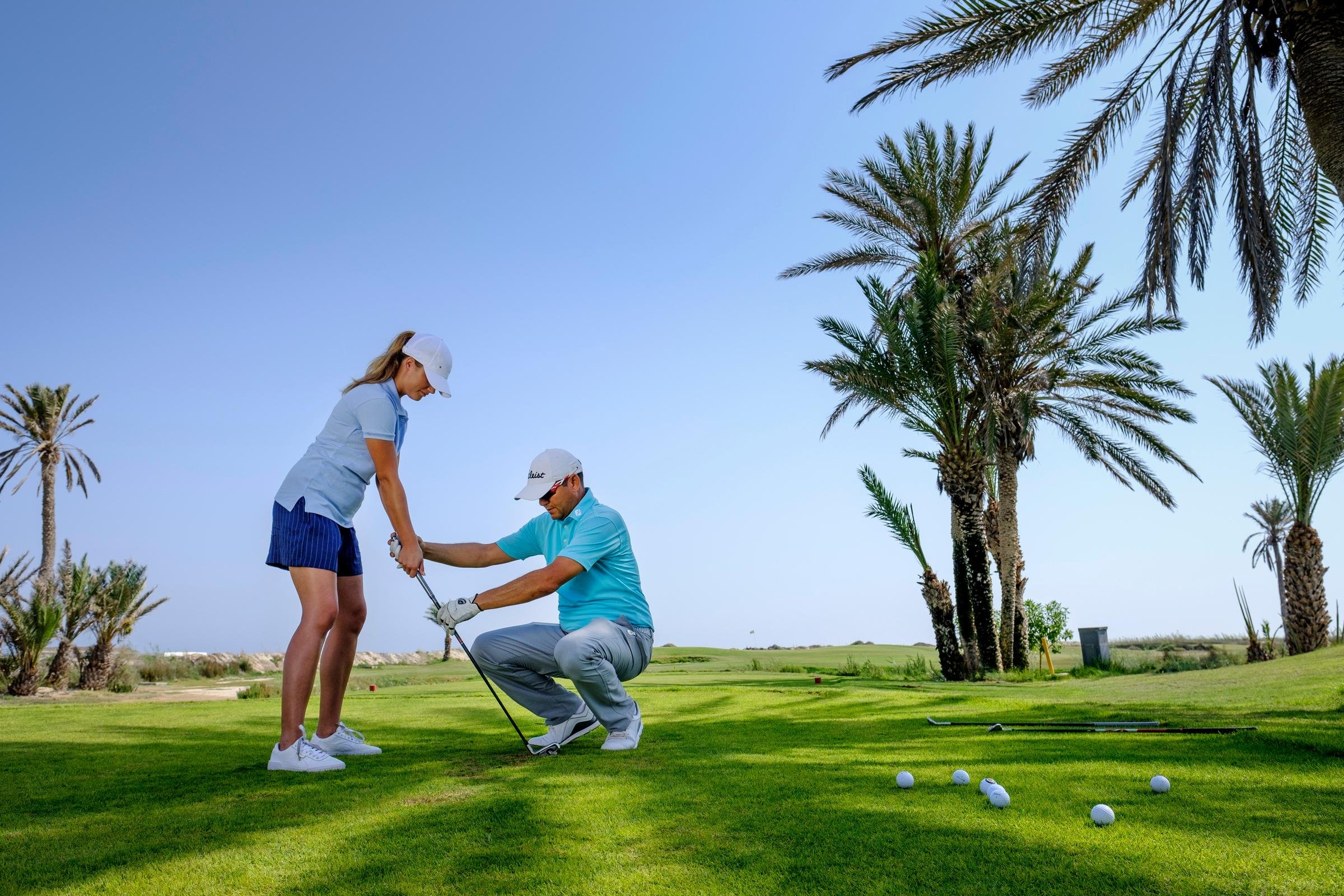 Zwei Personen beim Golftraining auf dem Golfplatz, Palmen im Hintergrund