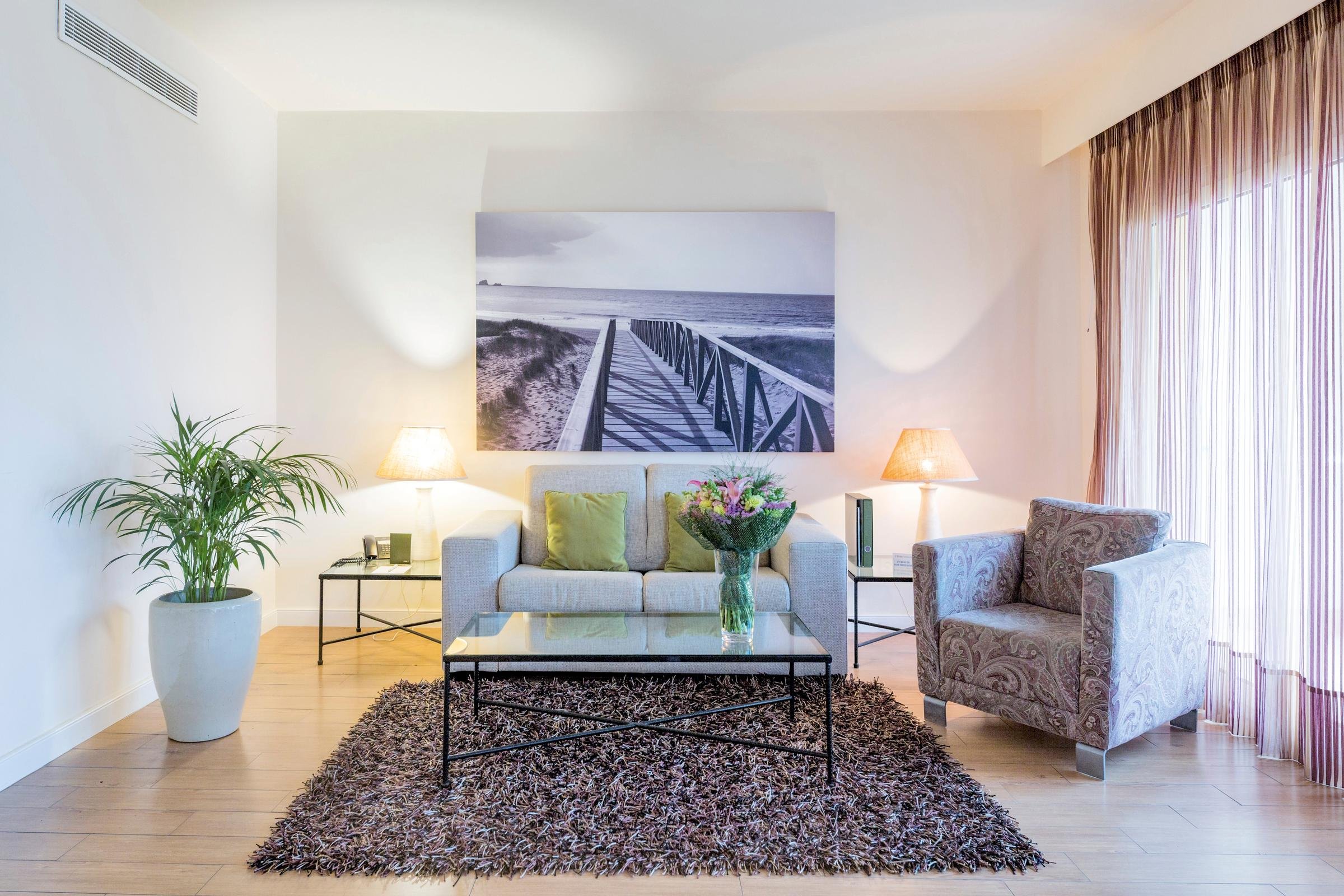 Gemütliches Wohnzimmer mit Sofa, Sessel, Pflanzen und Blick ins Licht durch Fenster