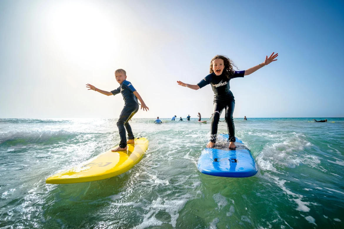 Zwei Kinder surfen auf dem Meer bei Sonnenaufgang, Spaß und Abenteuer im Premium Cluburlaub
