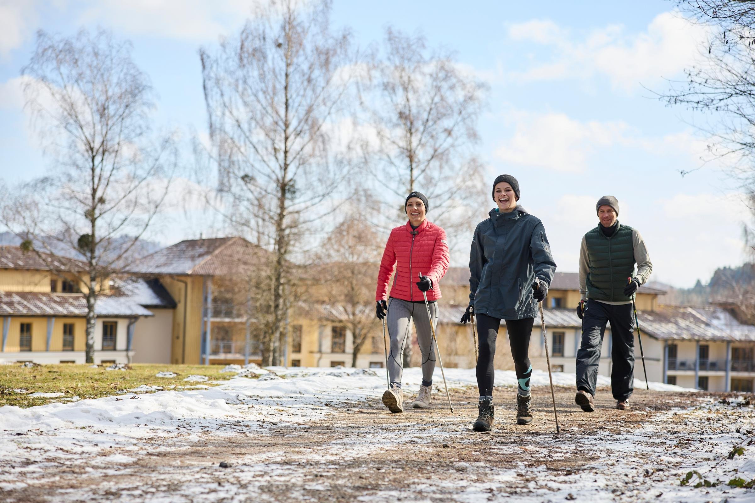 Vier Personen gehen im Winterkleidung auf einem unbefestigten Weg vor eleganten Gebäuden des Premium-Cluburlaubsanbieter Aldiana.