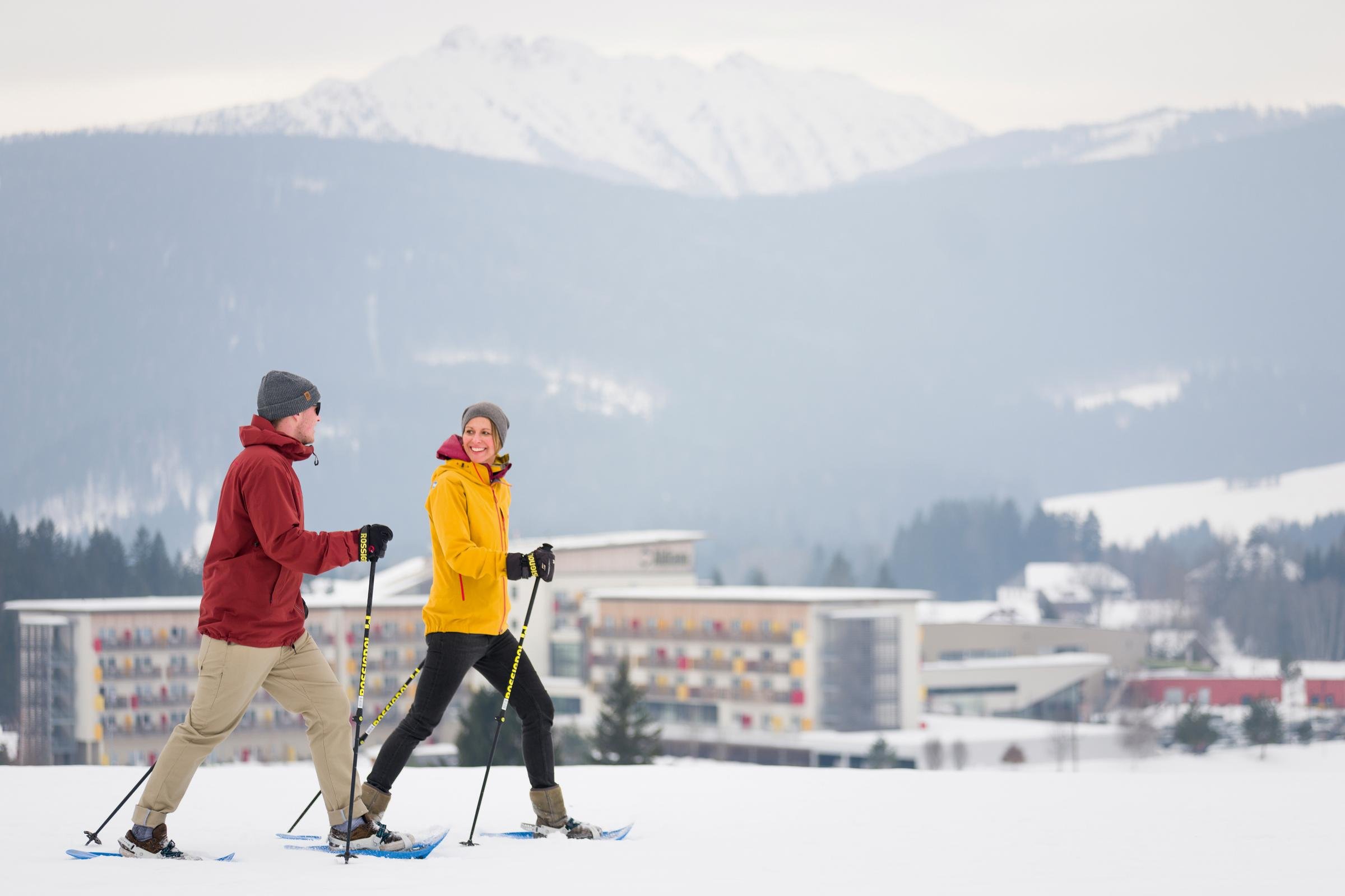 Zwei Skifahrer beim Sporturlaub in den Alpen, modernes Hotel im Hintergrund
